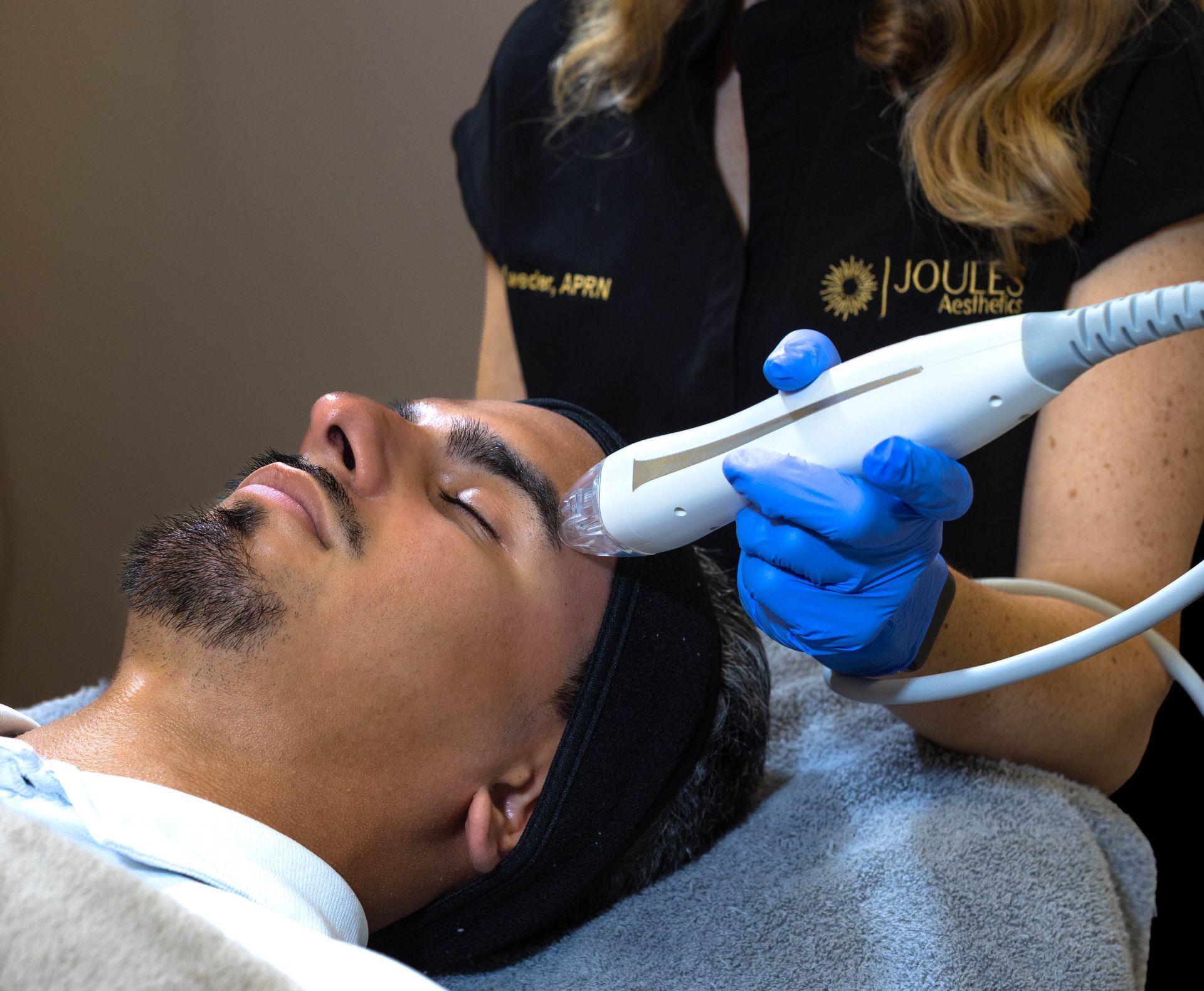 Man receiving facial treatment with a handheld device, in a spa setting.
