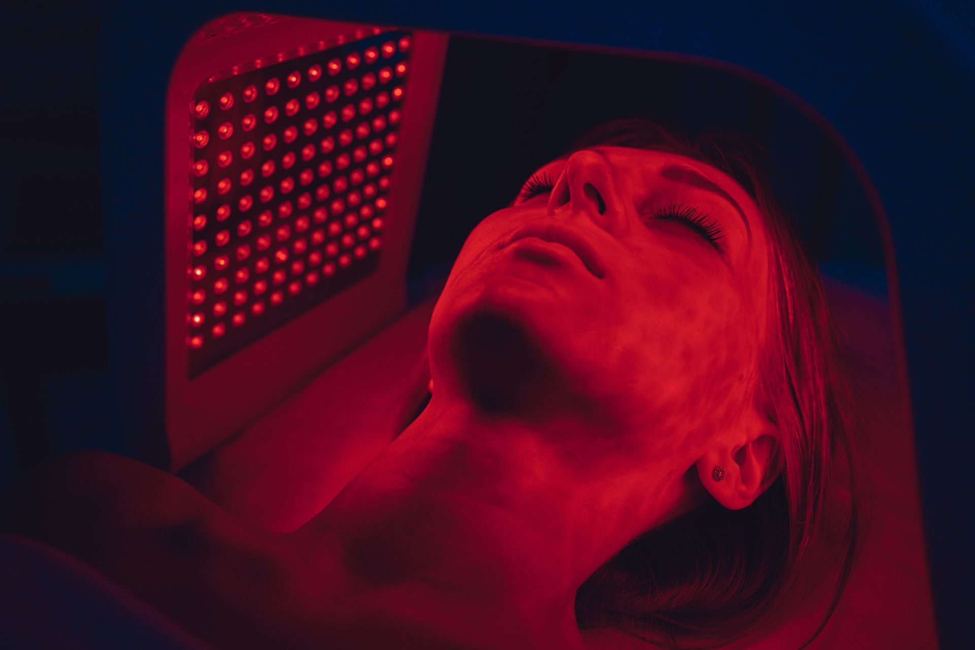 Woman lying under a red LED light therapy device for facial skin treatment.