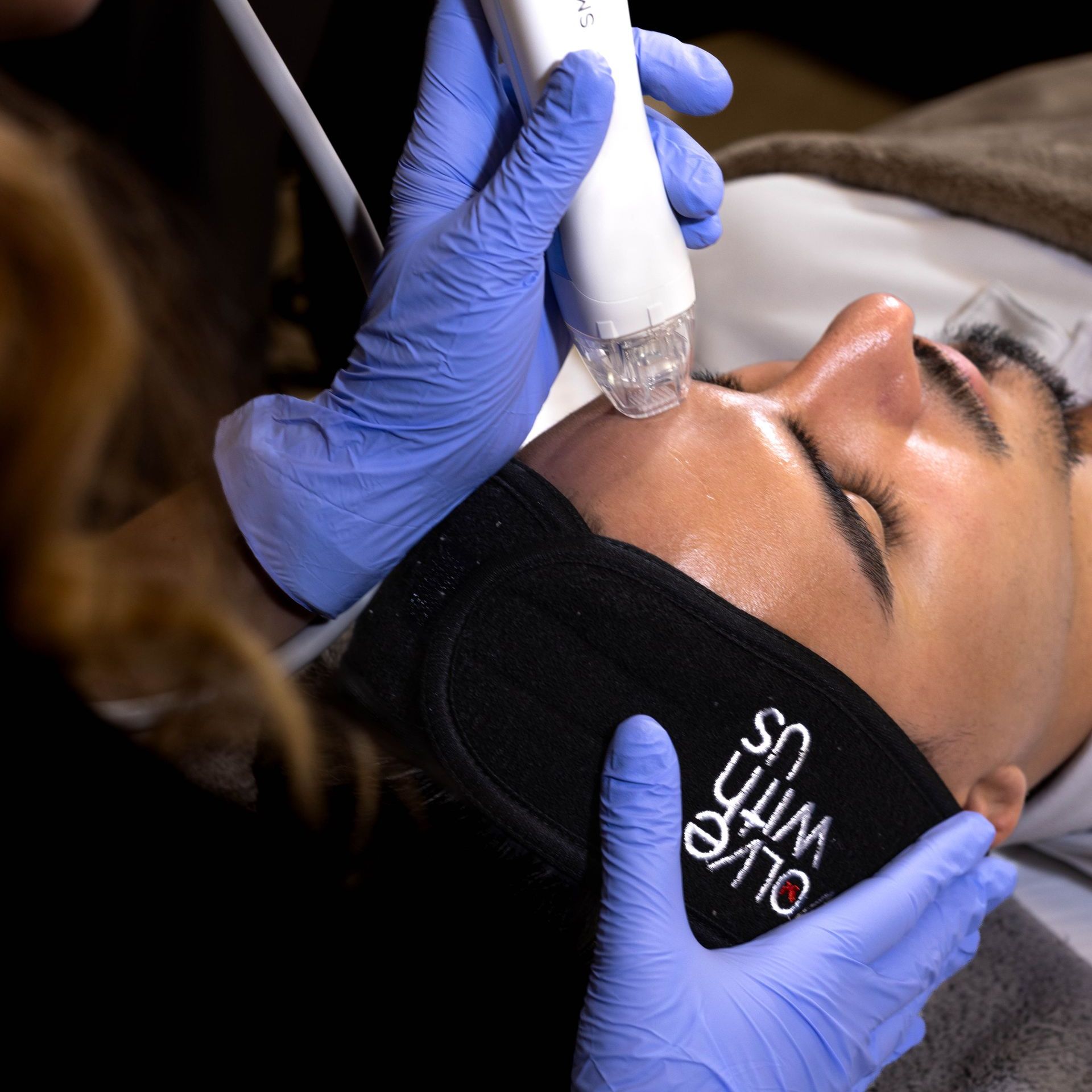 A man is getting a facial treatment from a woman wearing blue gloves.