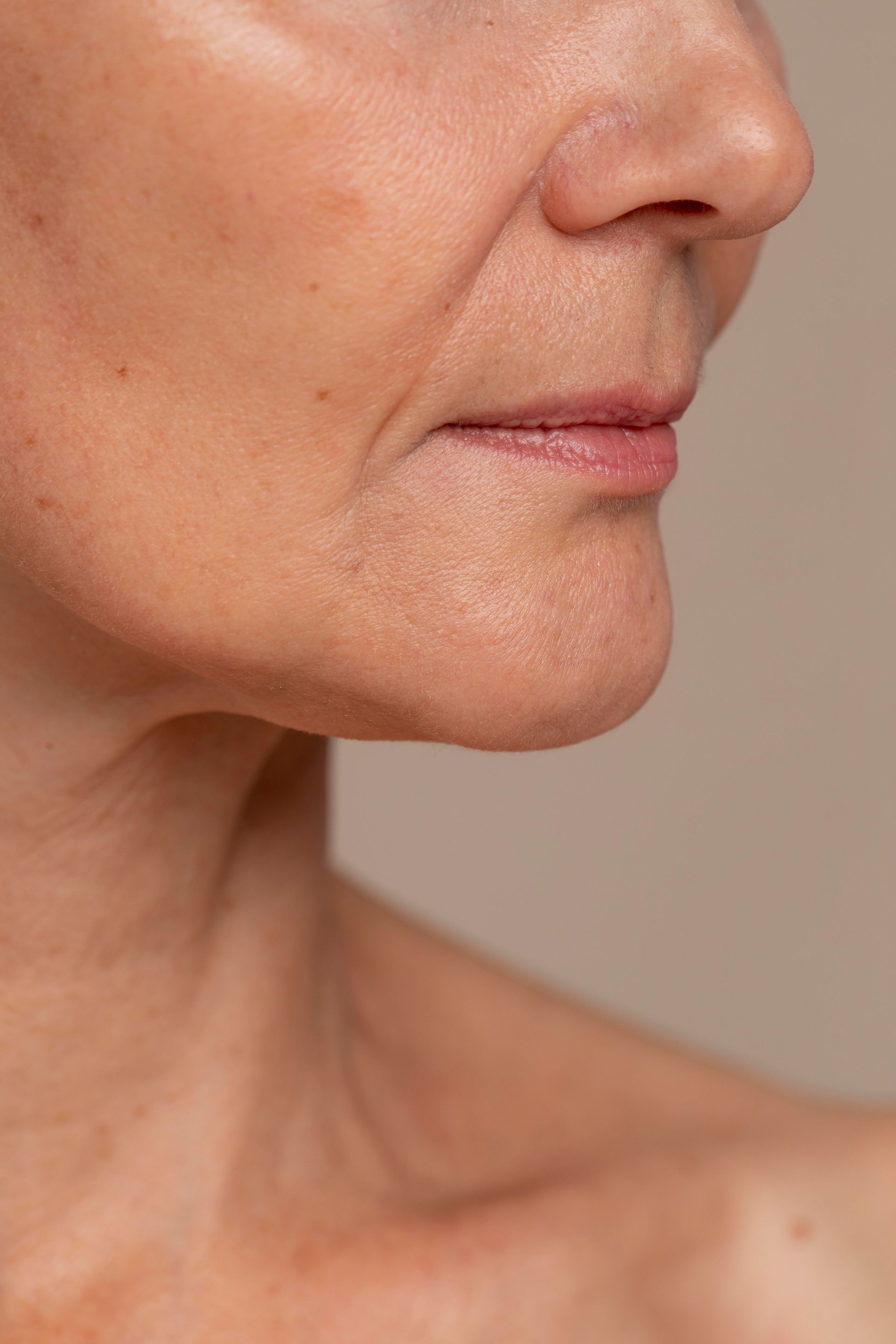 A close-up profile view of a human chin, jawline, and mouth against a plain, neutral background.