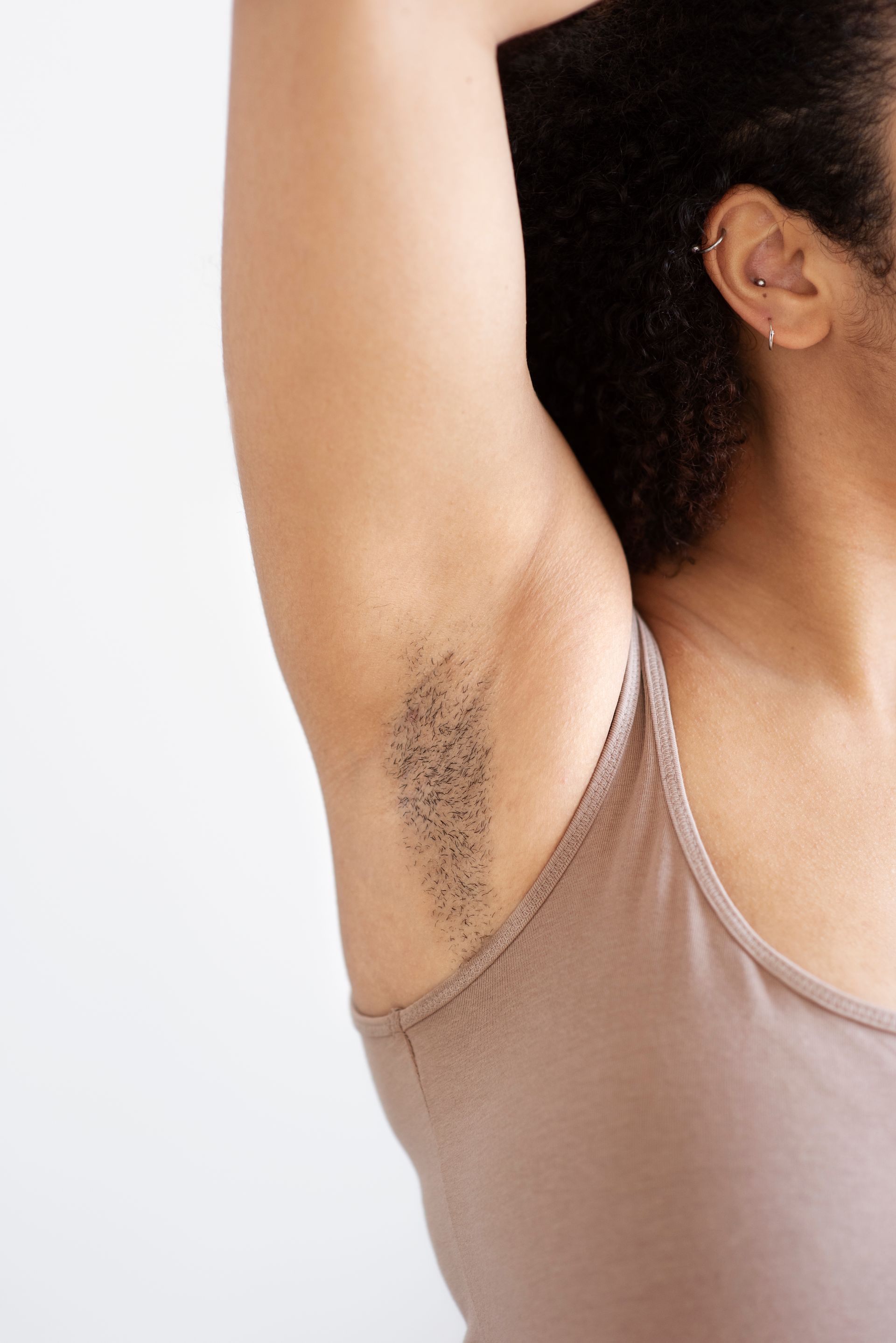 Close-up of an underarm with visible armpit hair on a person wearing a beige tank top.