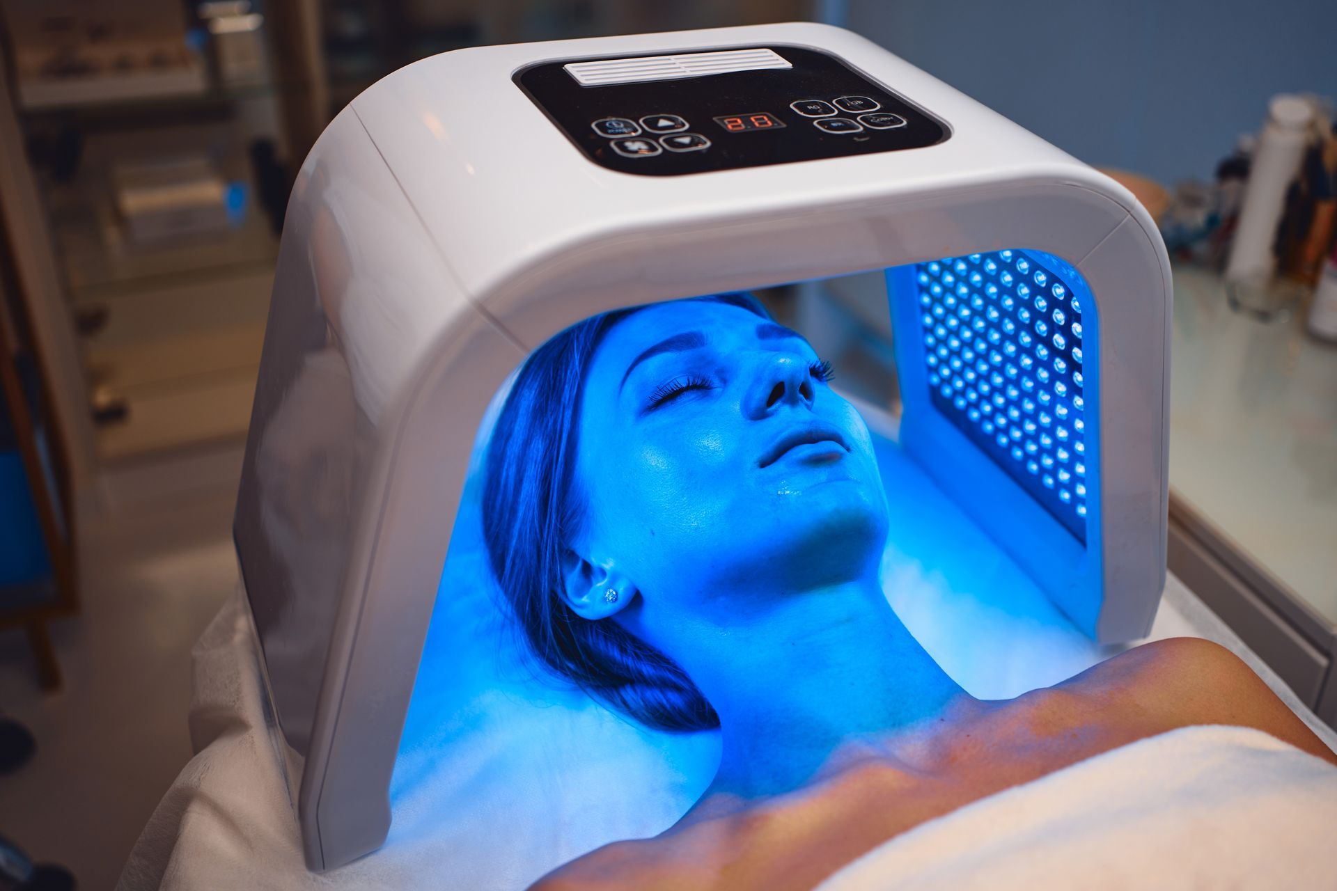 Woman undergoing blue light therapy for skin treatment. She is lying down with blue light shining on her face.