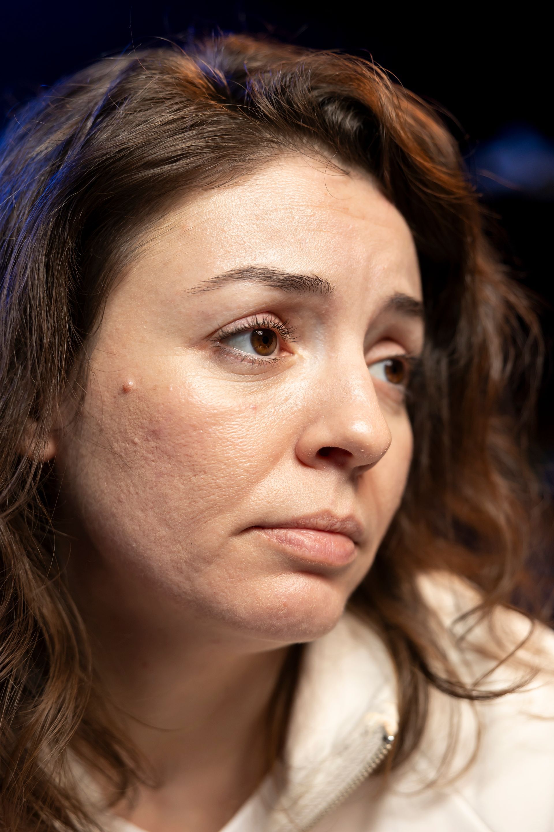 A close-up portrait of a person with brown hair and a neutral expression, looking slightly off-camera.