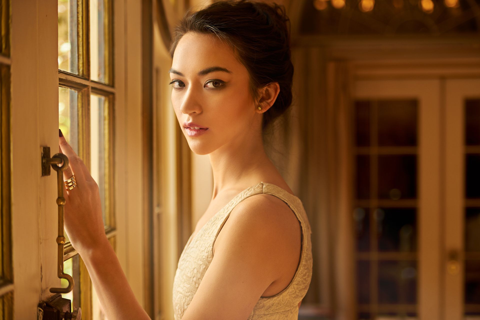 A woman in a white dress is standing in front of a window.