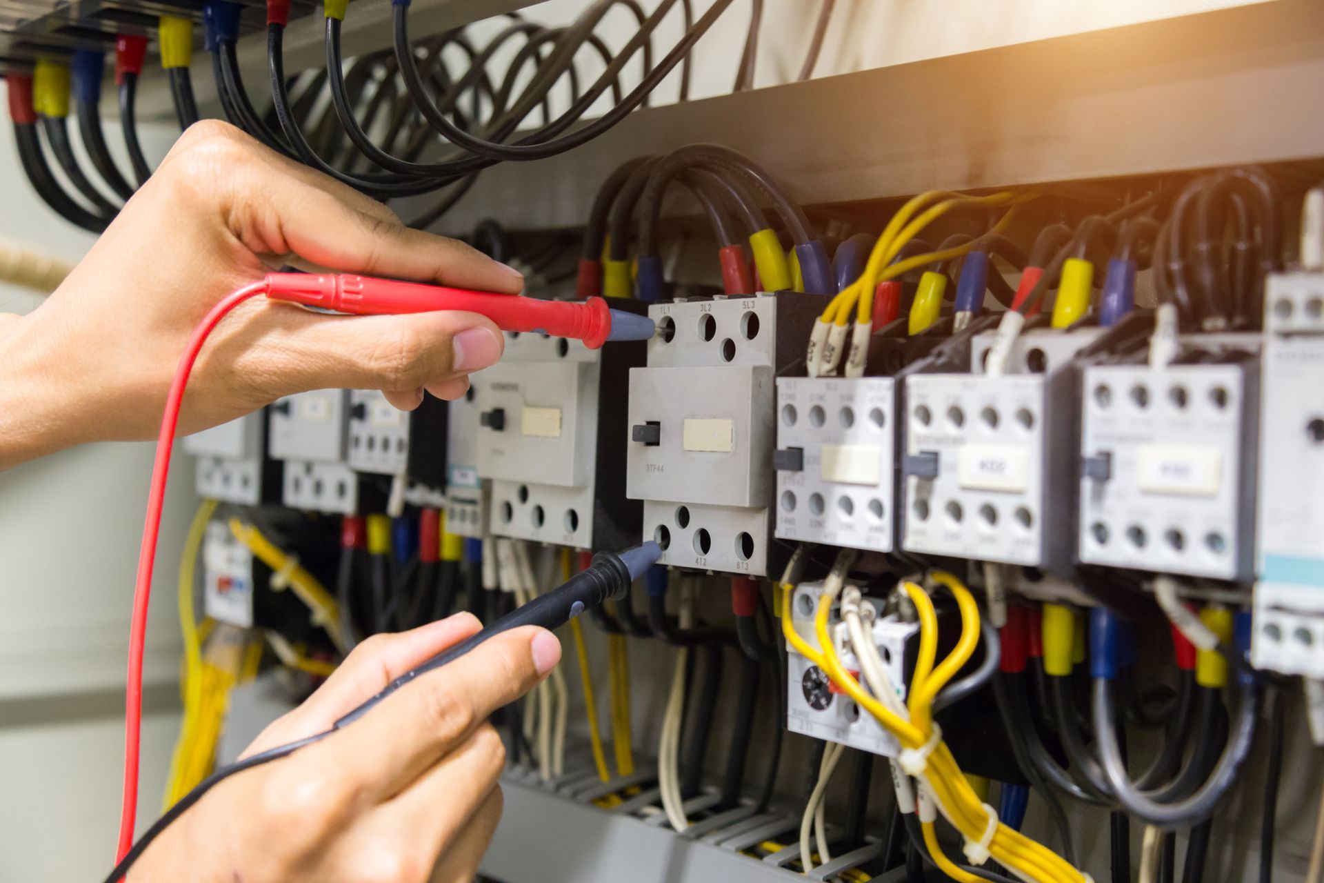 An electrician is working on an electrical panel with a multimeter.