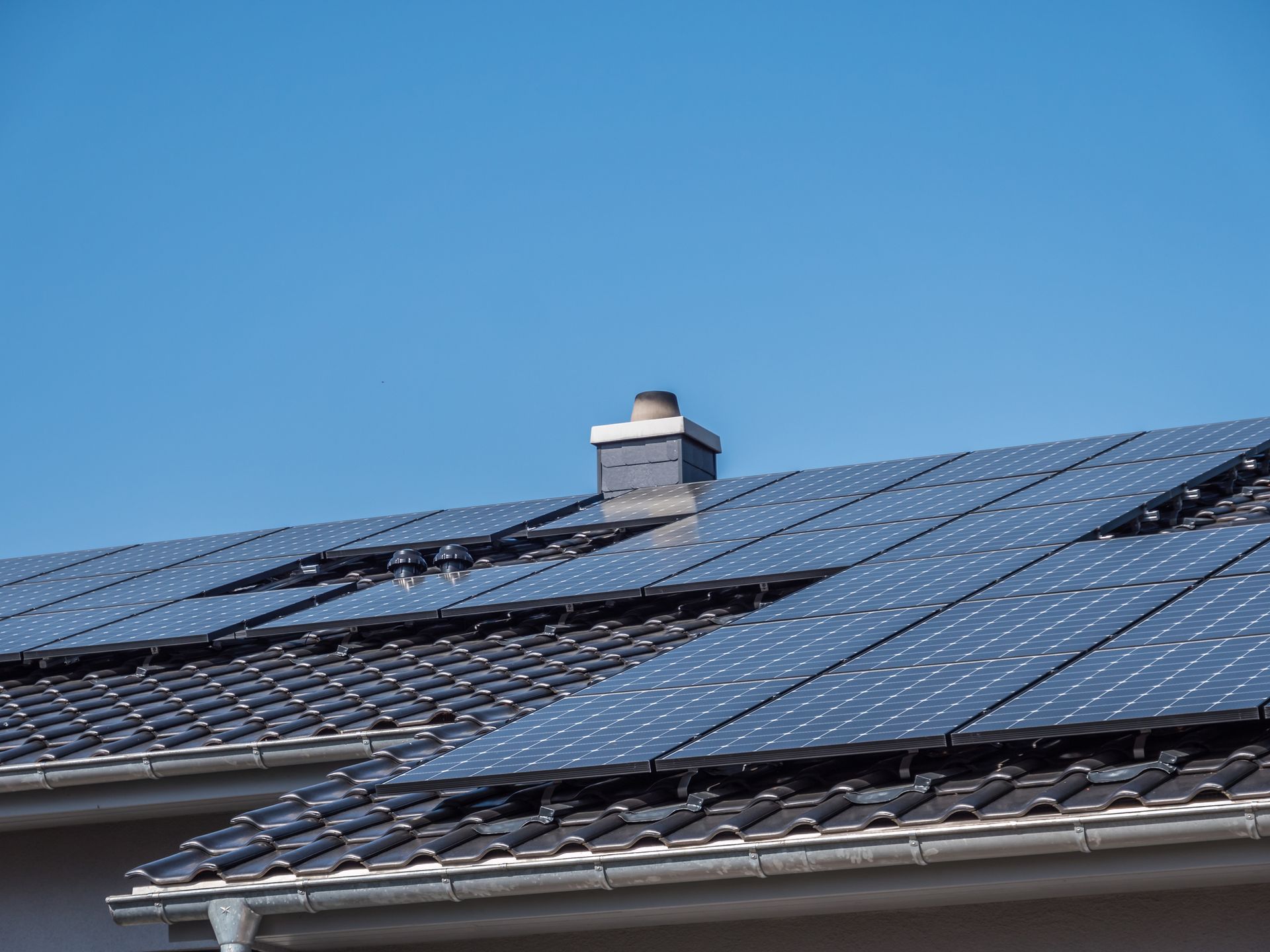 Solar panels on a rooftop with a chimney, against a clear blue sky.
