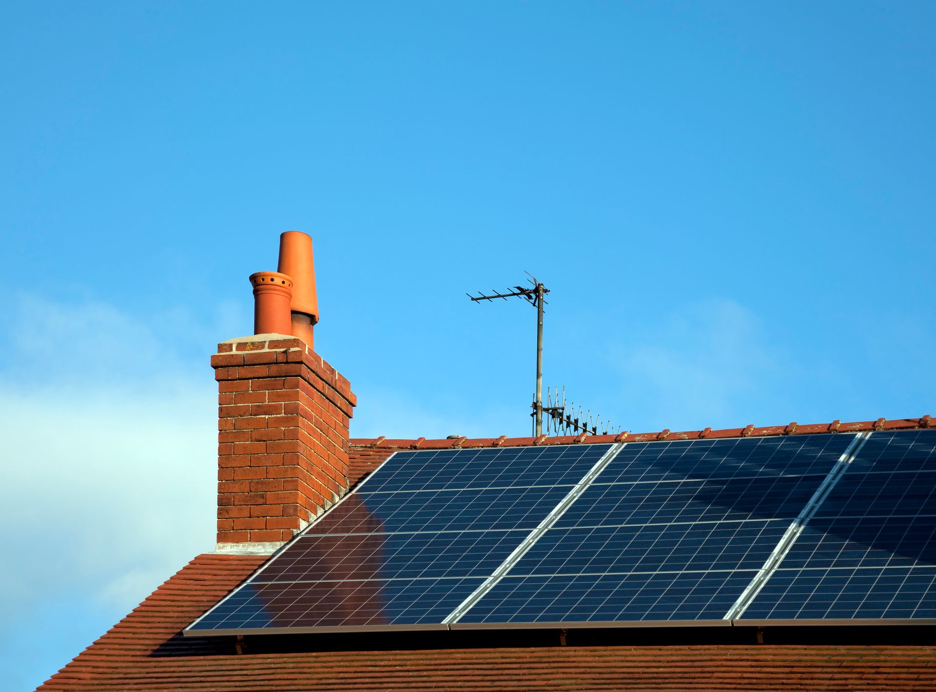 Roof with solar panels, chimney, and antenna against a blue sky.