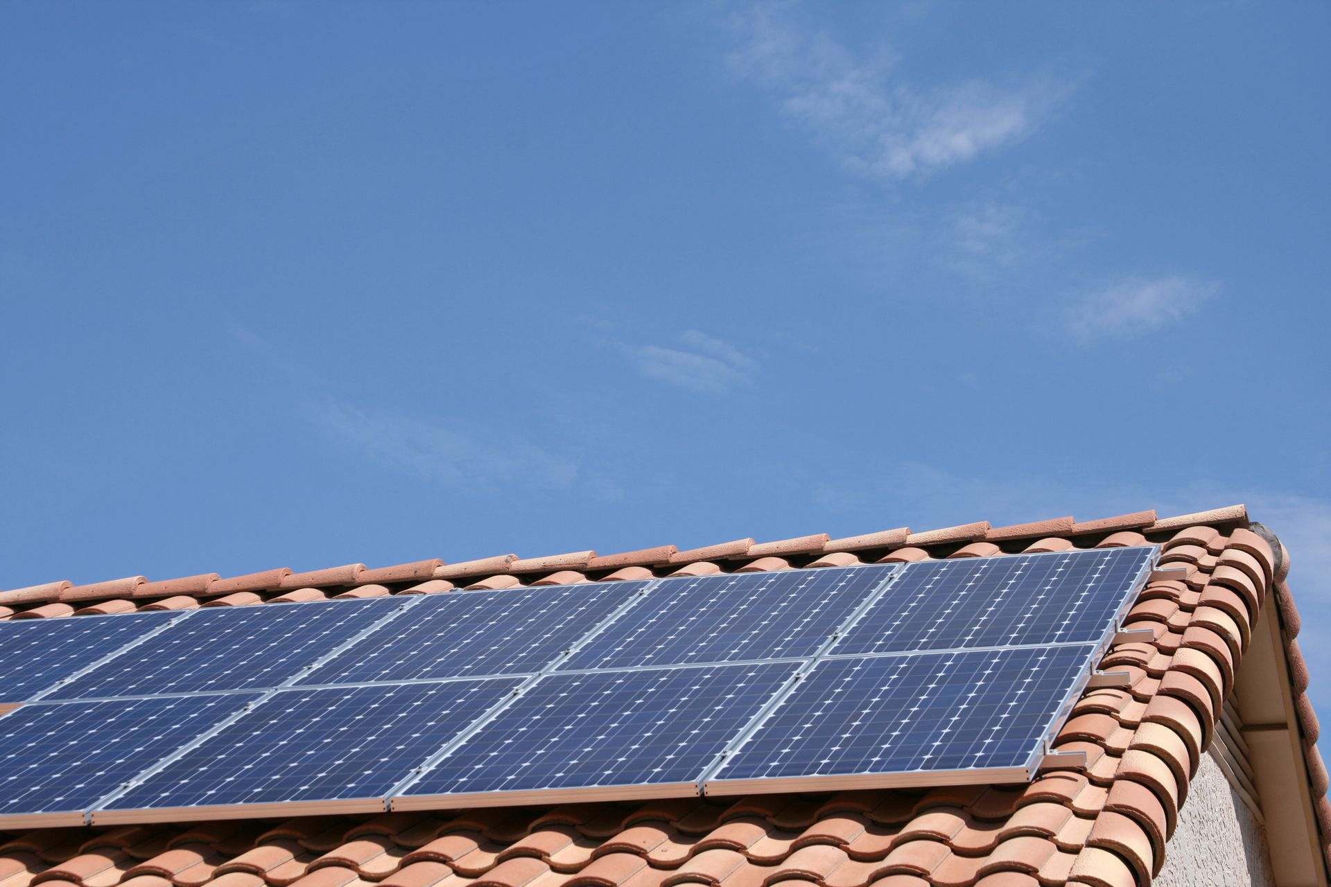 Solar panels on a red-tiled roof against a clear blue sky.