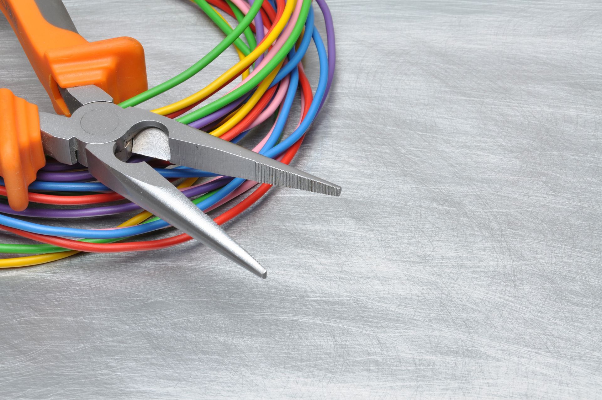 Pliers with orange handles on a coil of colorful electrical wires, on a gray surface.