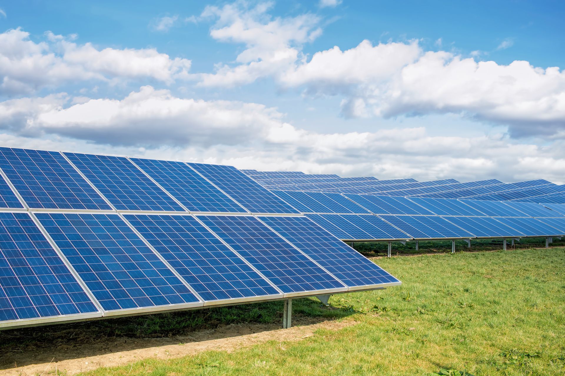 Solar panels in a field under a cloudy blue sky.