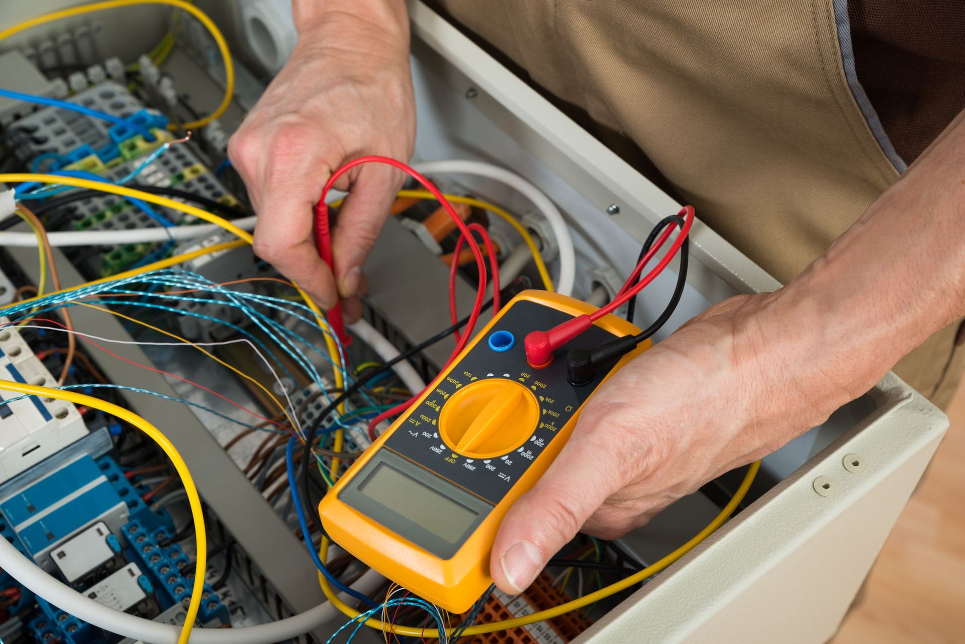Electrician using a multimeter to test wires inside an electrical panel.