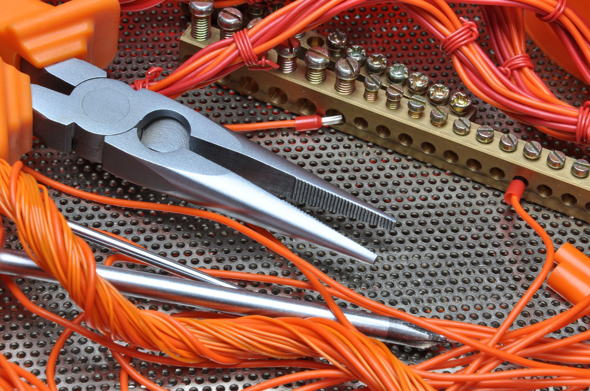 Pliers, orange wires, and electrical components on a metal surface, suggesting electrical work.