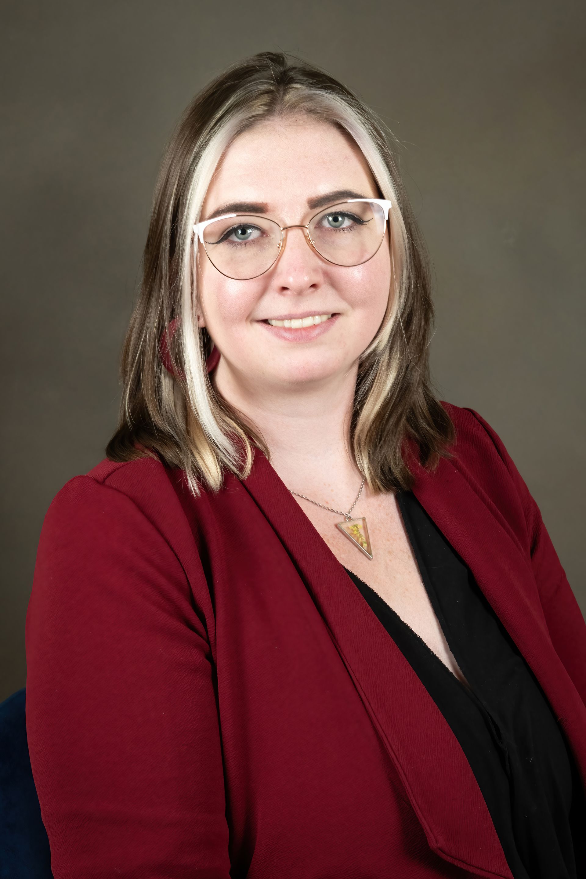 A woman wearing glasses and a red jacket is smiling for the camera.