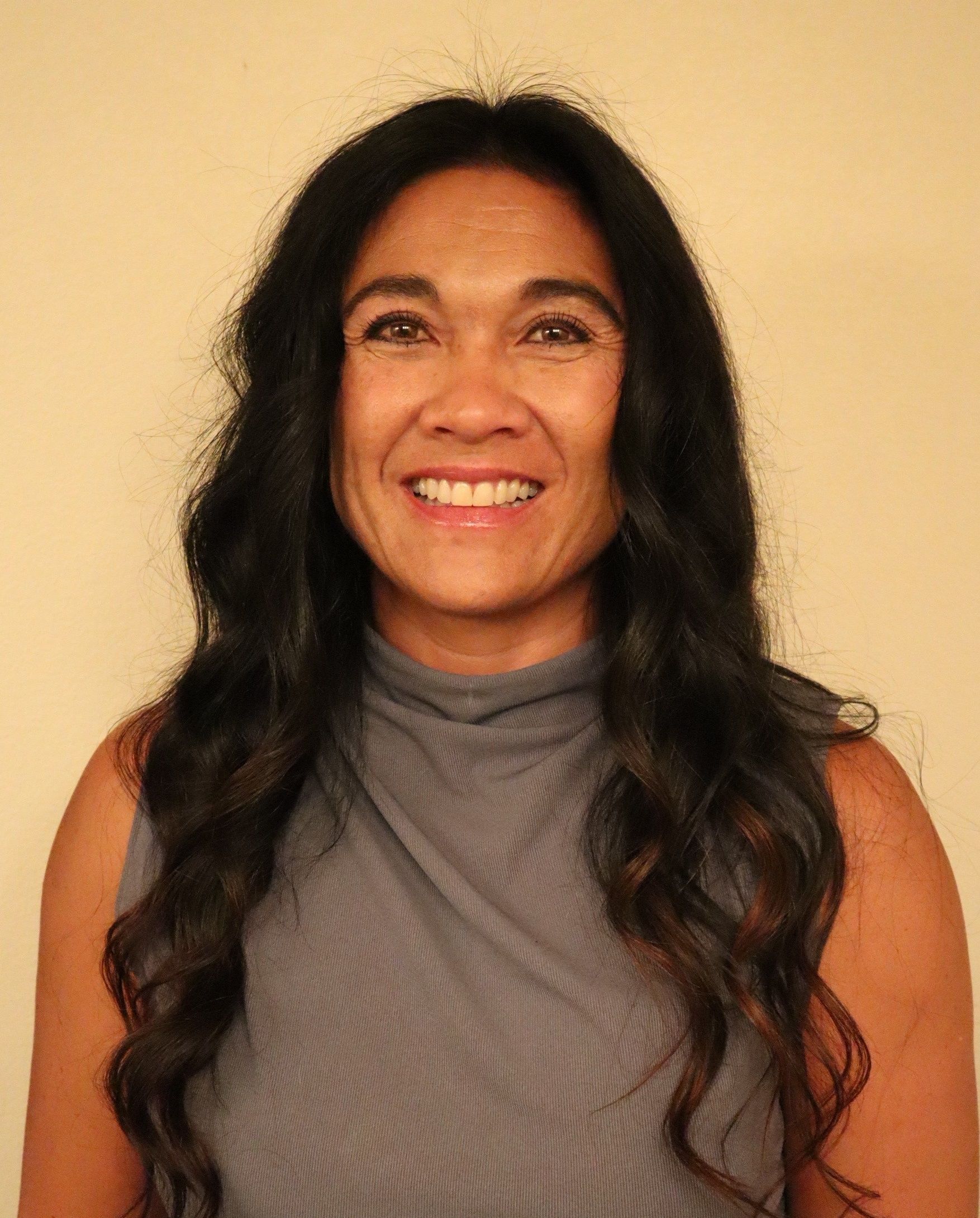 A woman wearing a necklace and earrings is standing in front of a yellow background.