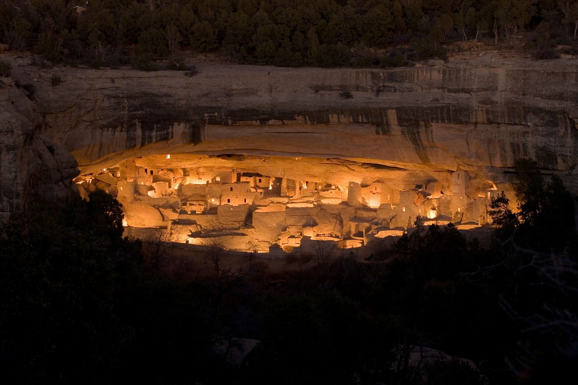 A large cave is lit up at night in the middle of a forest.