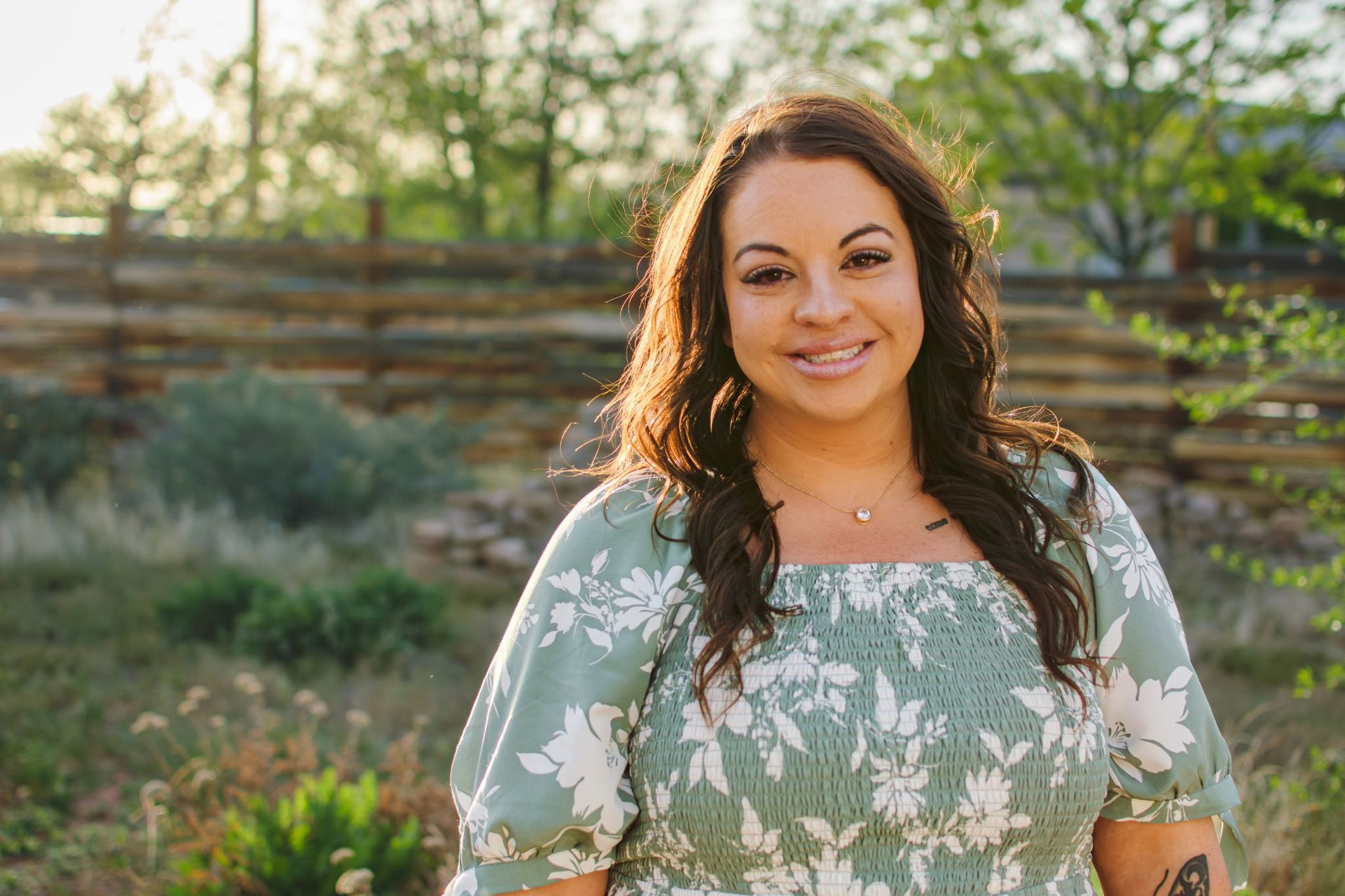 A woman wearing a necklace and earrings is standing in front of a yellow background.