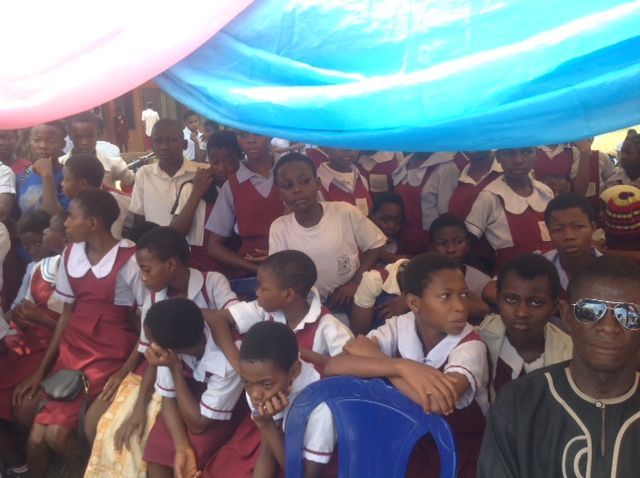 A group of children are sitting under a blue tarp