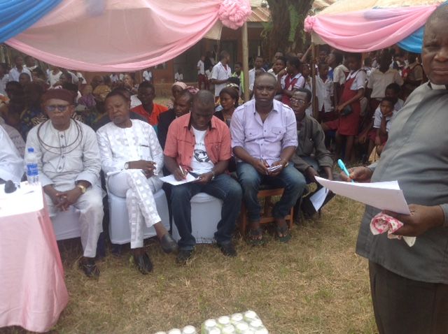 A man is holding a piece of paper in front of a crowd of people sitting in chairs.