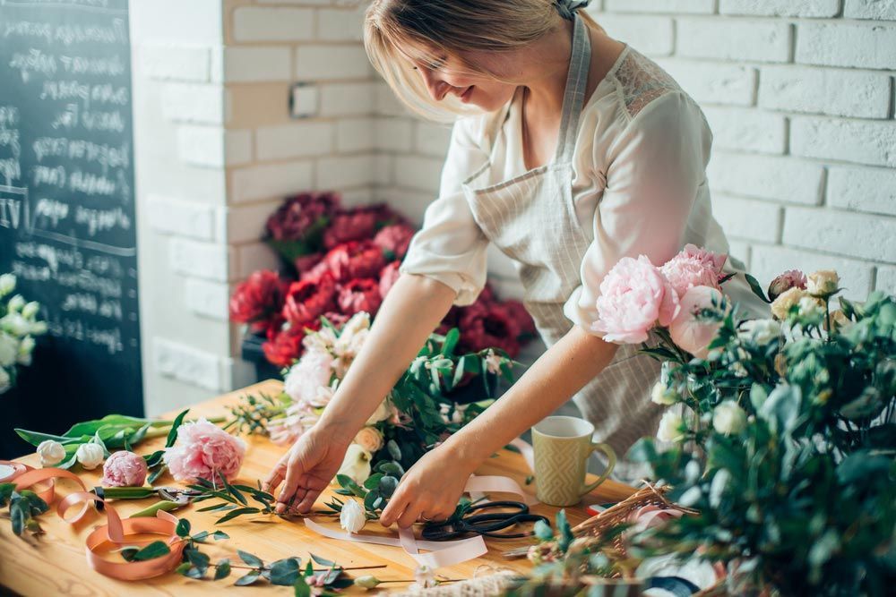 A Woman is Making a Bouquet of Flowers on a Wooden Table — Castletown Flower Hut in Pimlico, QLD
