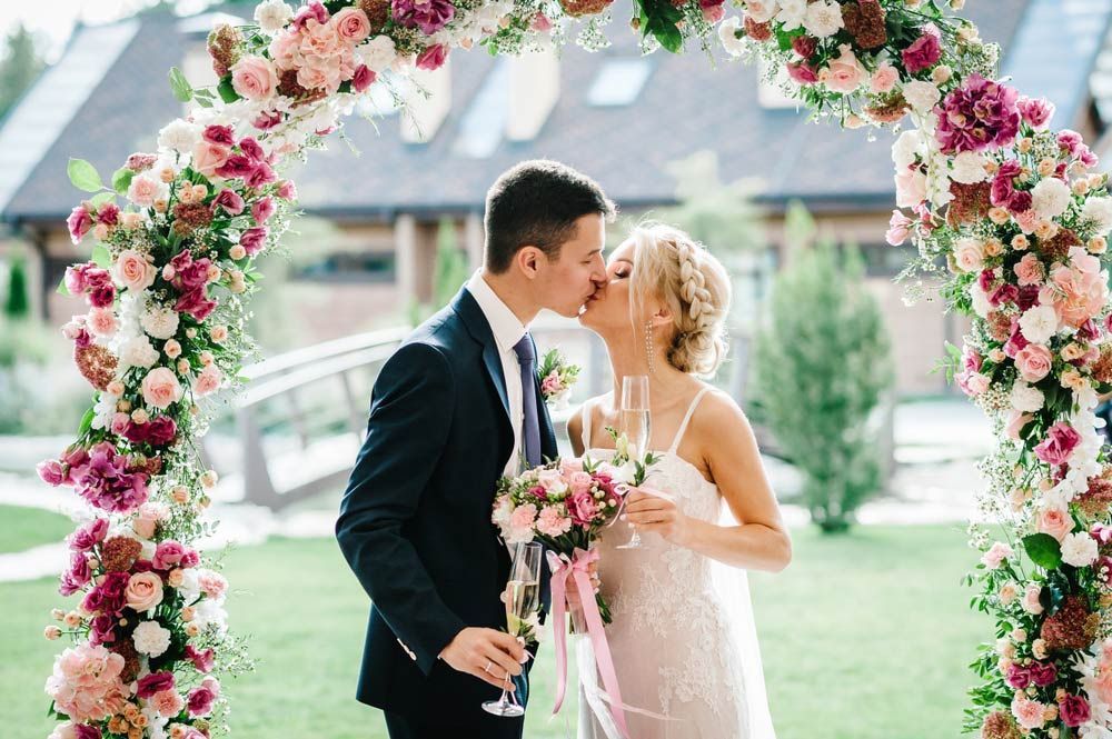 A Bride and Groom Are Kissing Under a Floral Arch at Their Wedding — Castletown Flower Hut in Pimlico, QLD