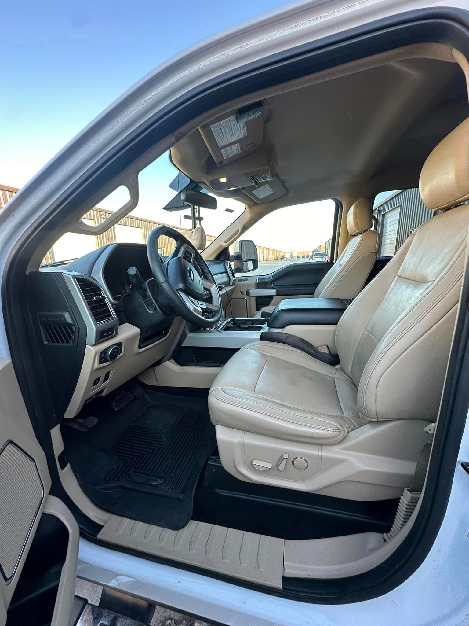 Interior of a beige leather-seated truck, including steering wheel, dashboard, and black floor mats.