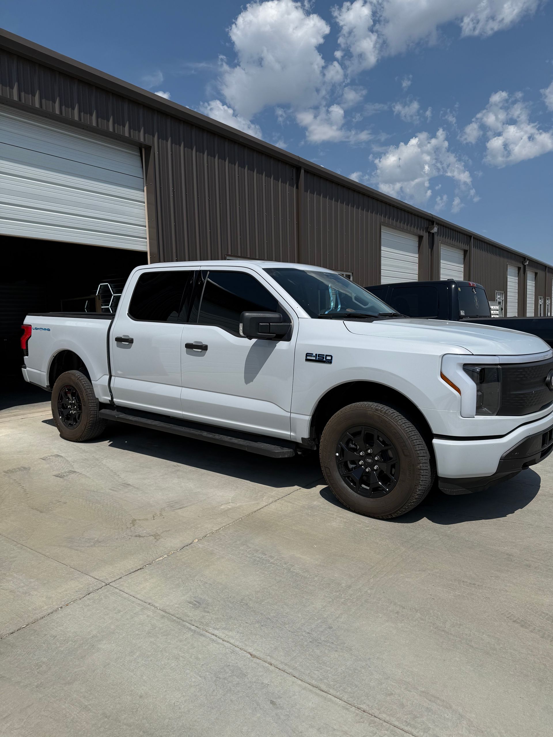 White Ford F-150 Lightning electric truck parked in front of a building with open garage doors on a sunny day.
