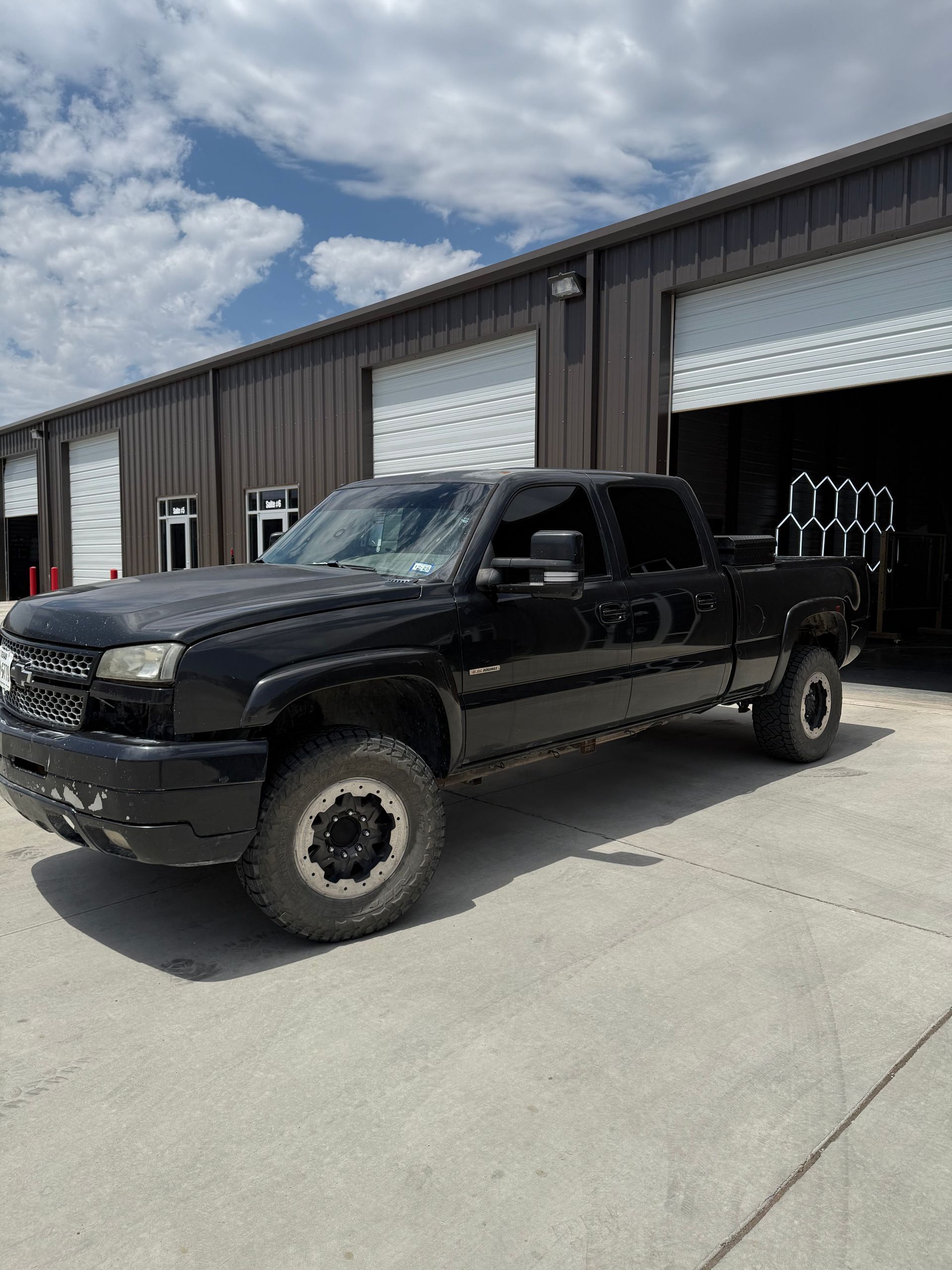 Black Chevy pickup truck parked in front of a metal building with open garage door.