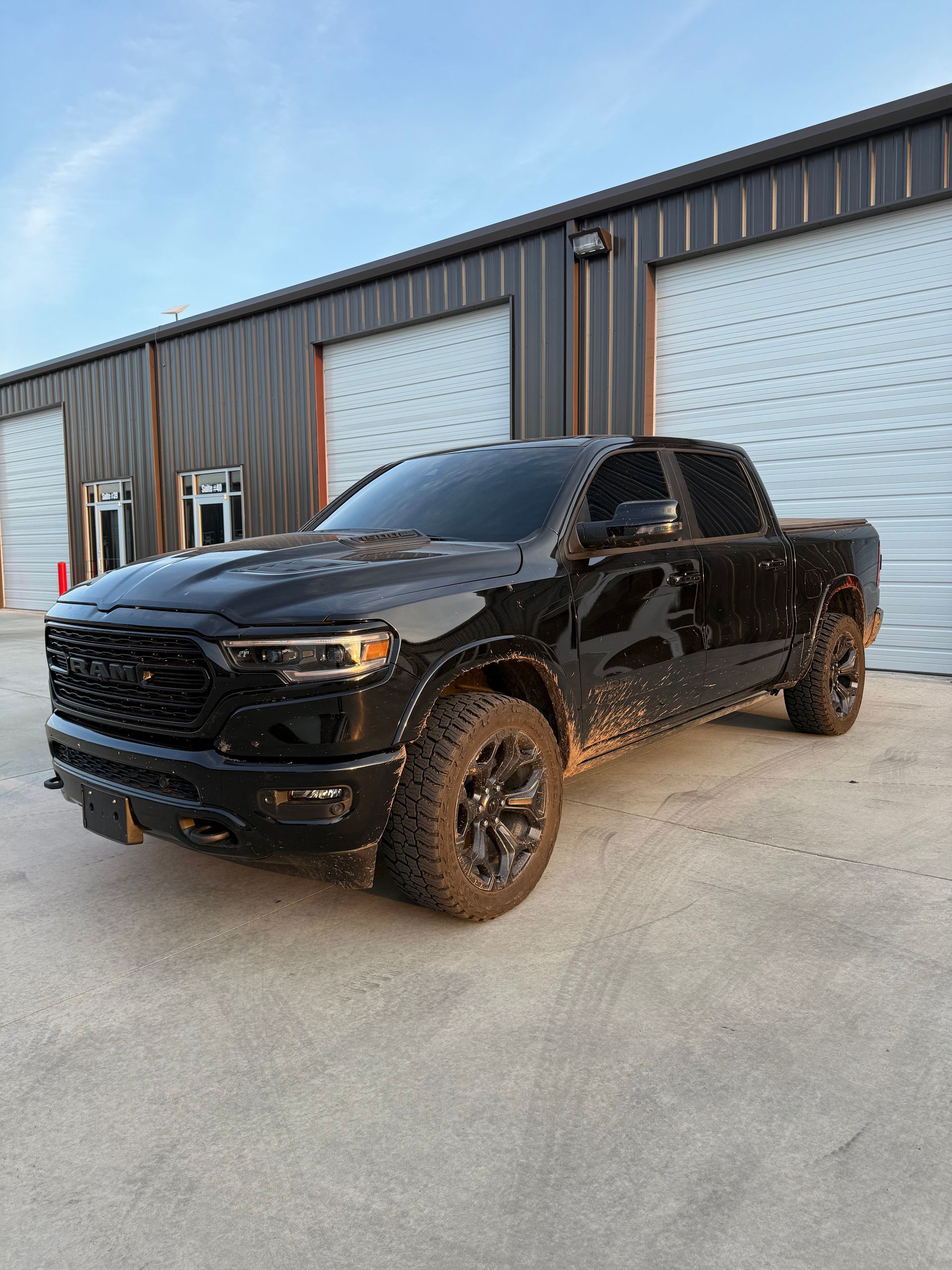 Black pickup truck parked outside a garage. The truck has mud on the side.