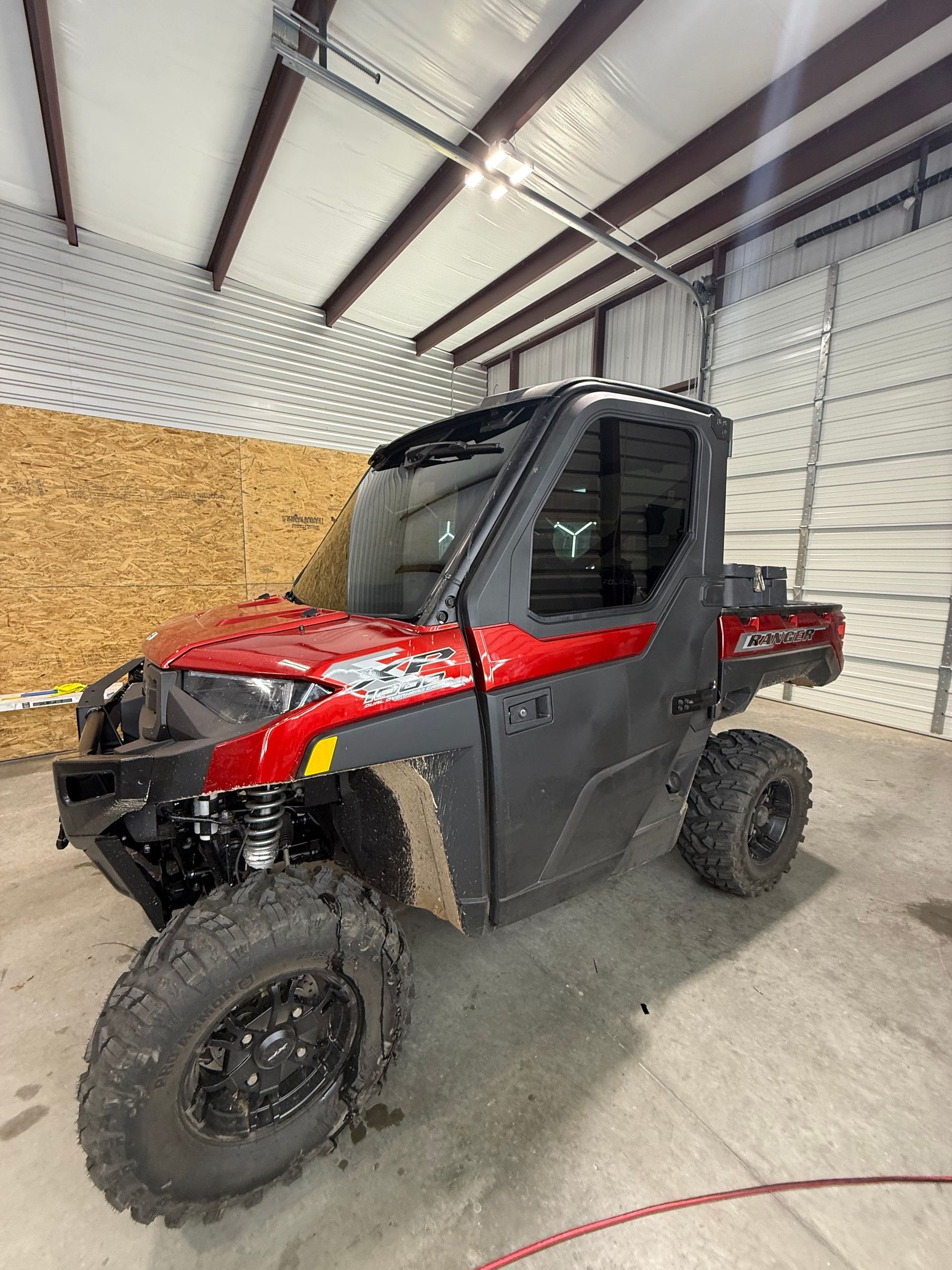 Red and black UTV inside a garage. It has large tires and a windshield.