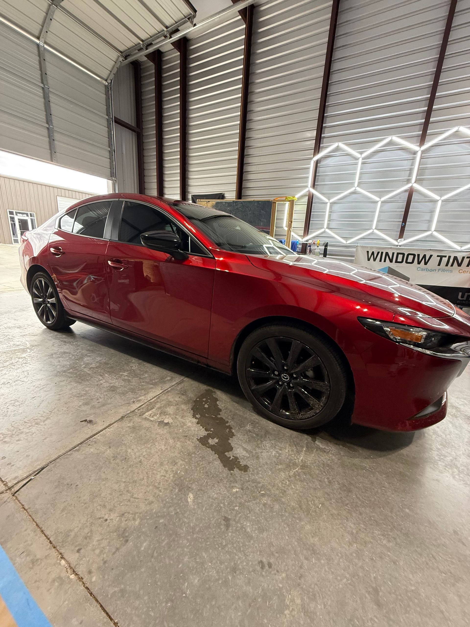 Red Mazda sedan with tinted windows parked in a garage. Black wheels.
