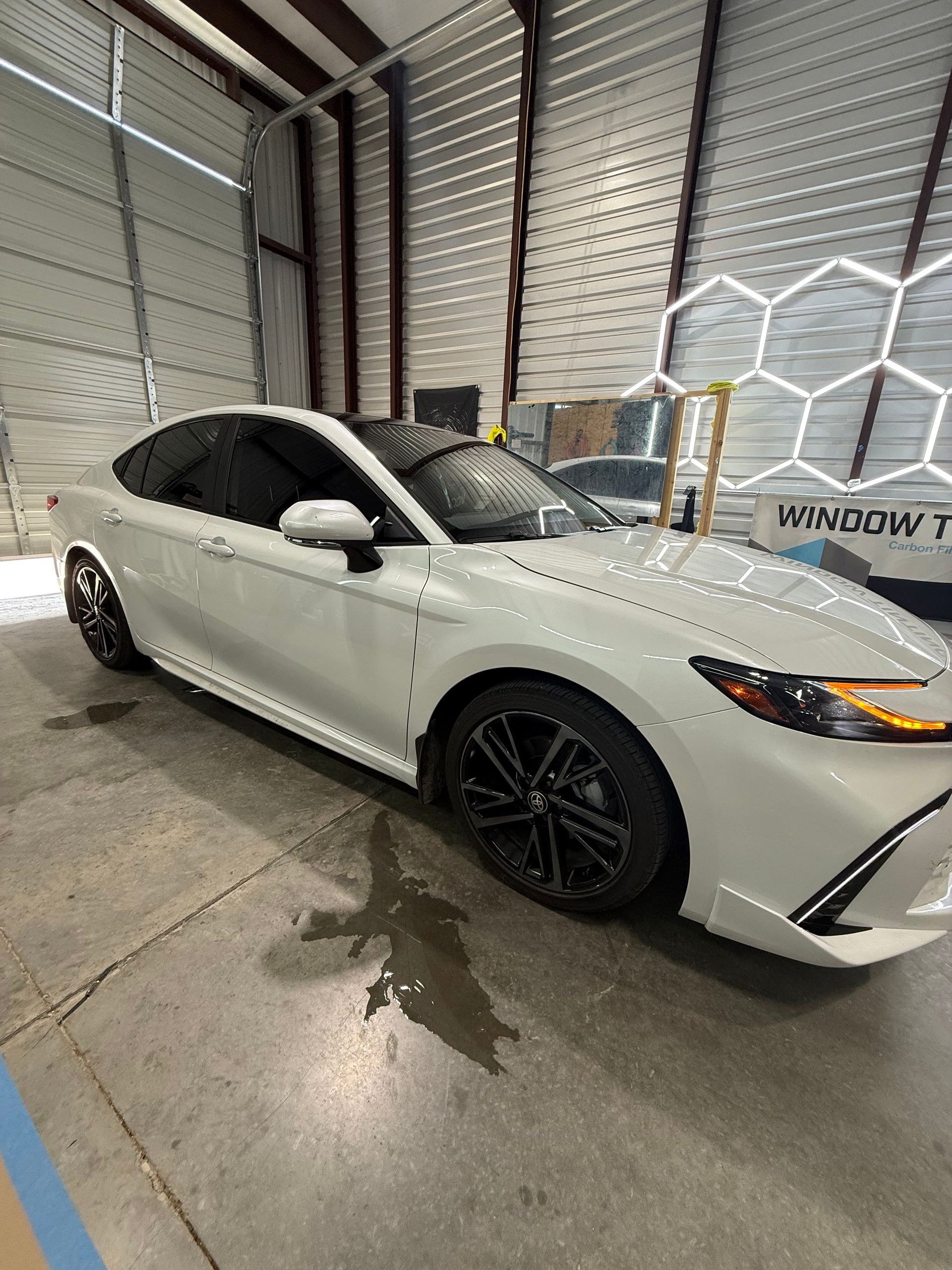 White Toyota Camry with tinted windows parked in a garage.