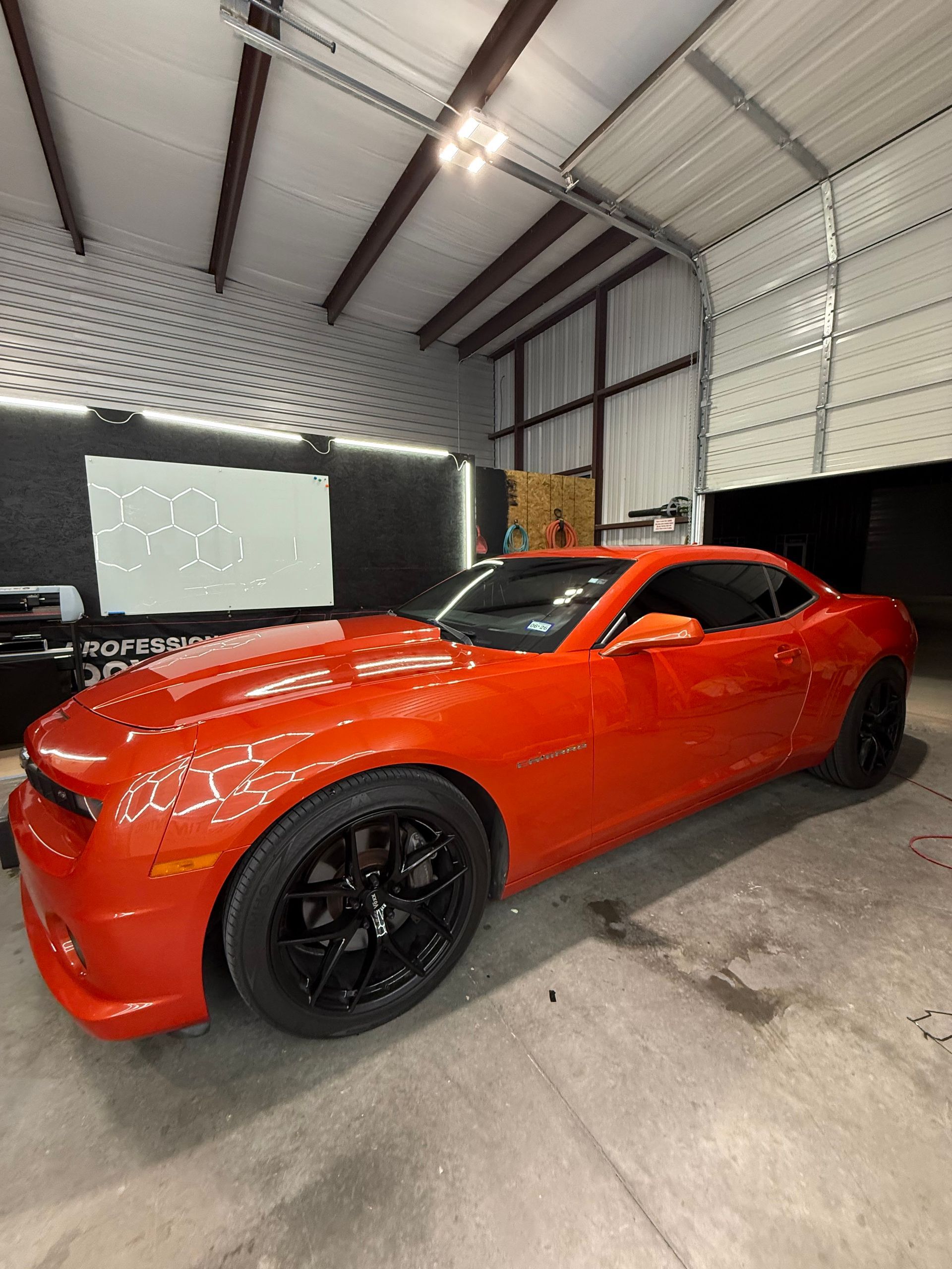 Orange sports car inside a garage with black rims, under ceiling lights.