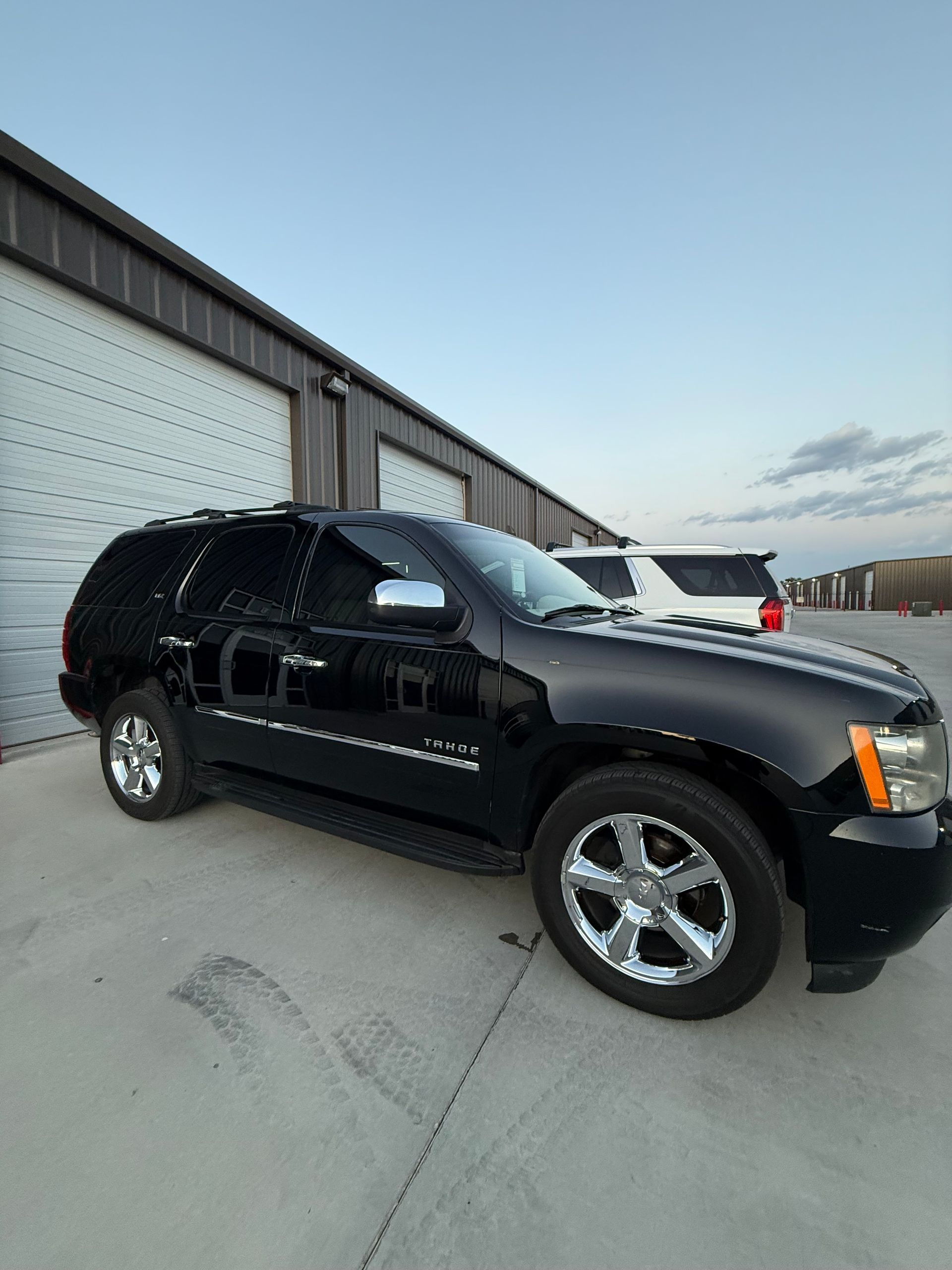 Black Chevrolet Tahoe SUV parked outside a building with white garage doors, under a blue sky.