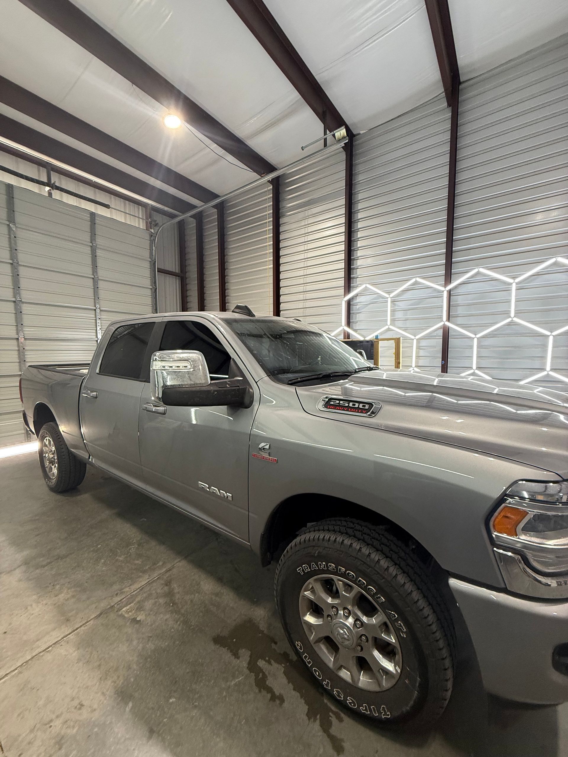 Silver Dodge Ram pickup truck inside a garage with hexagonal patterned wall.