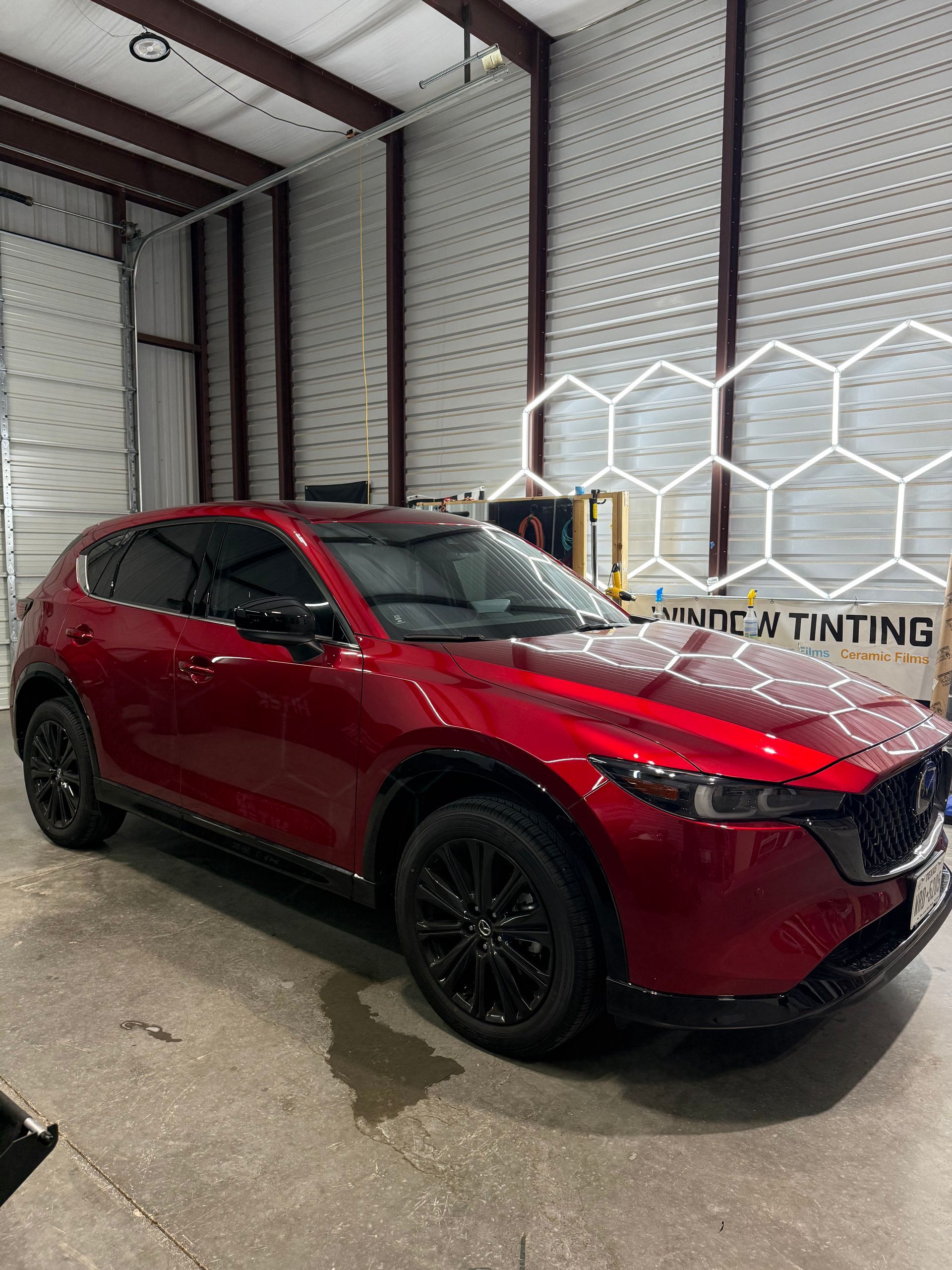 Red Mazda CX-5 SUV with black wheels, tinted windows, in a garage setting with LED honeycomb lights.