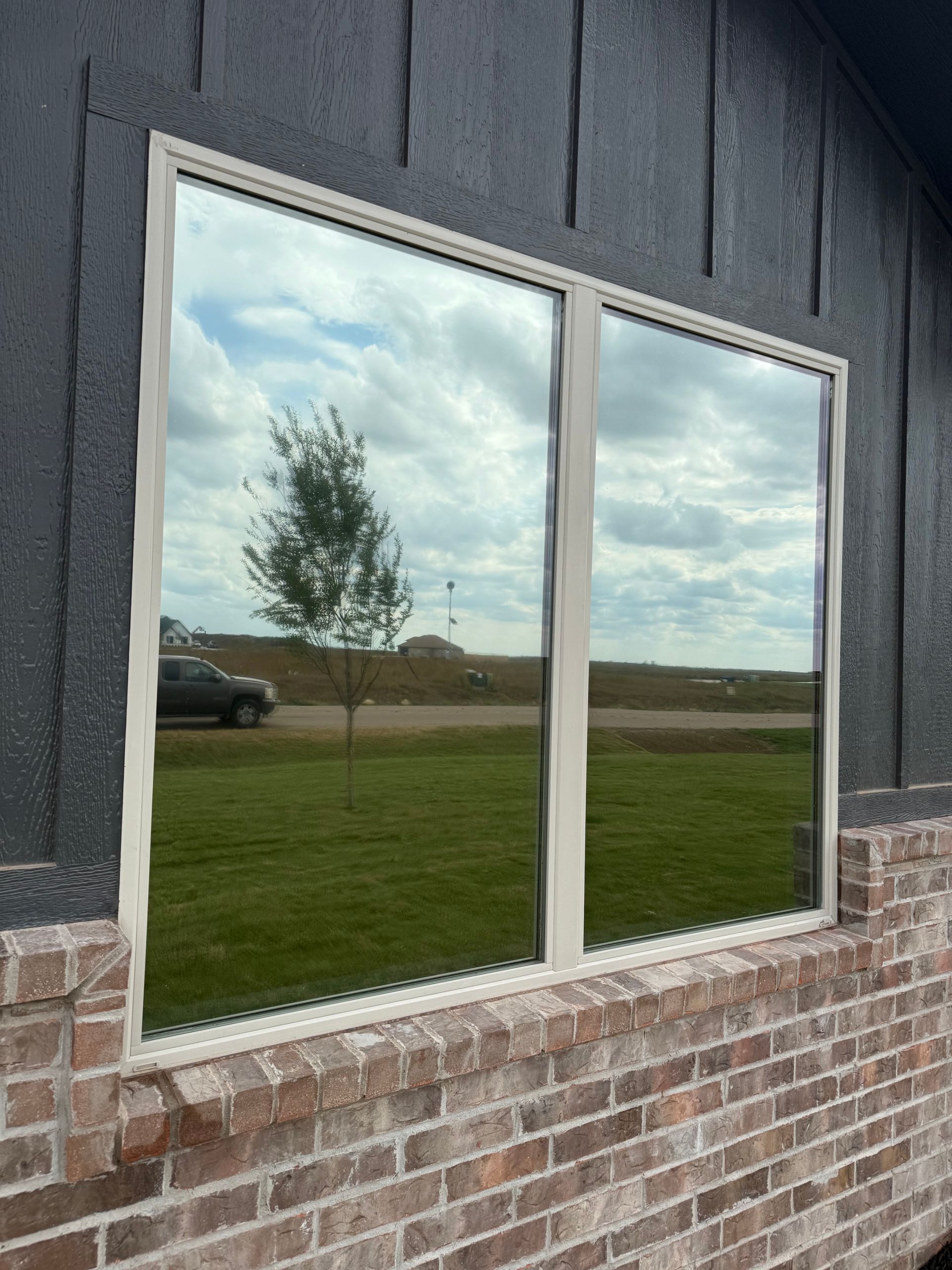 Reflective window on brick building. Sky and landscape visible in the glass.