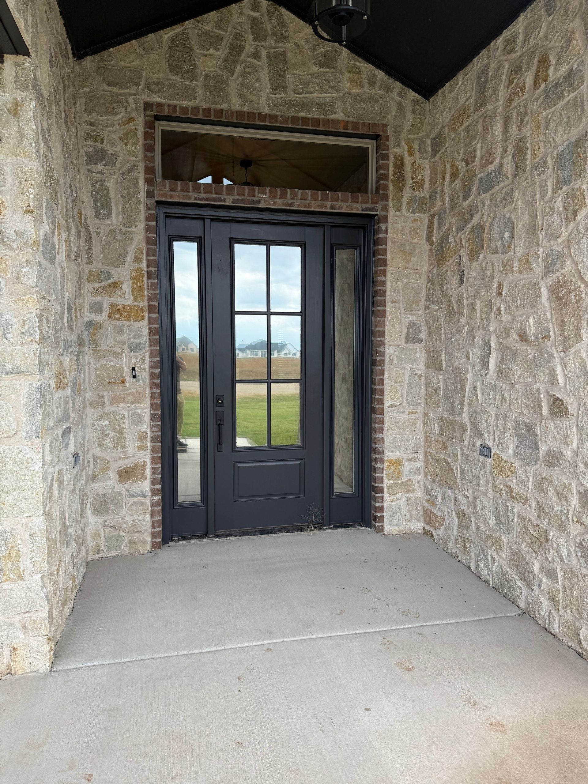 Stone facade entrance with black door, sidelights, and transom window. Concrete porch.