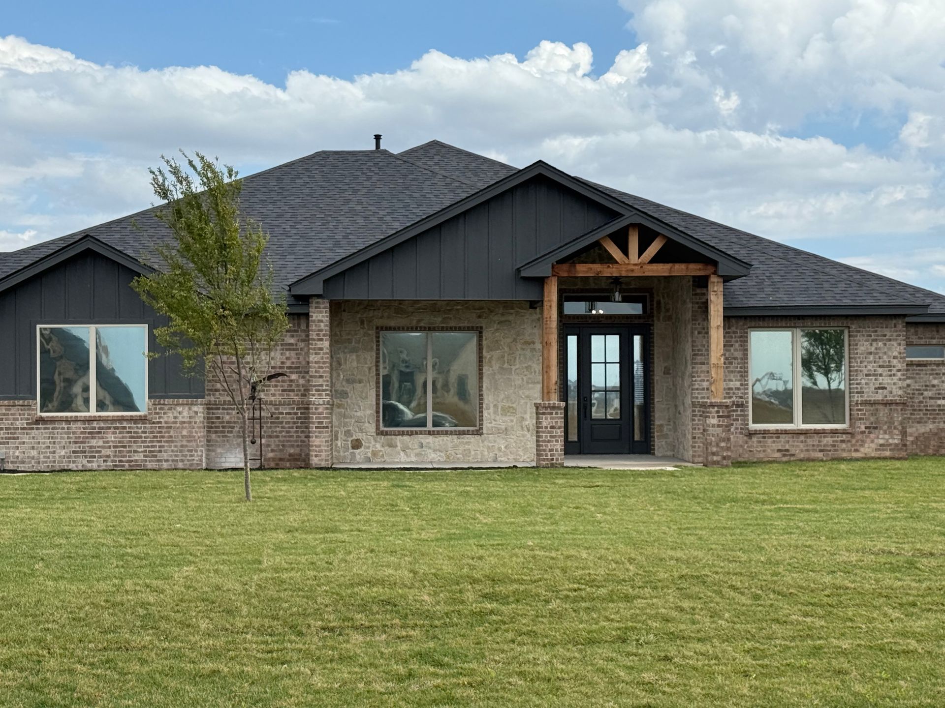 Brick house with dark roof and trim, wooden entrance, and large windows on a green lawn.