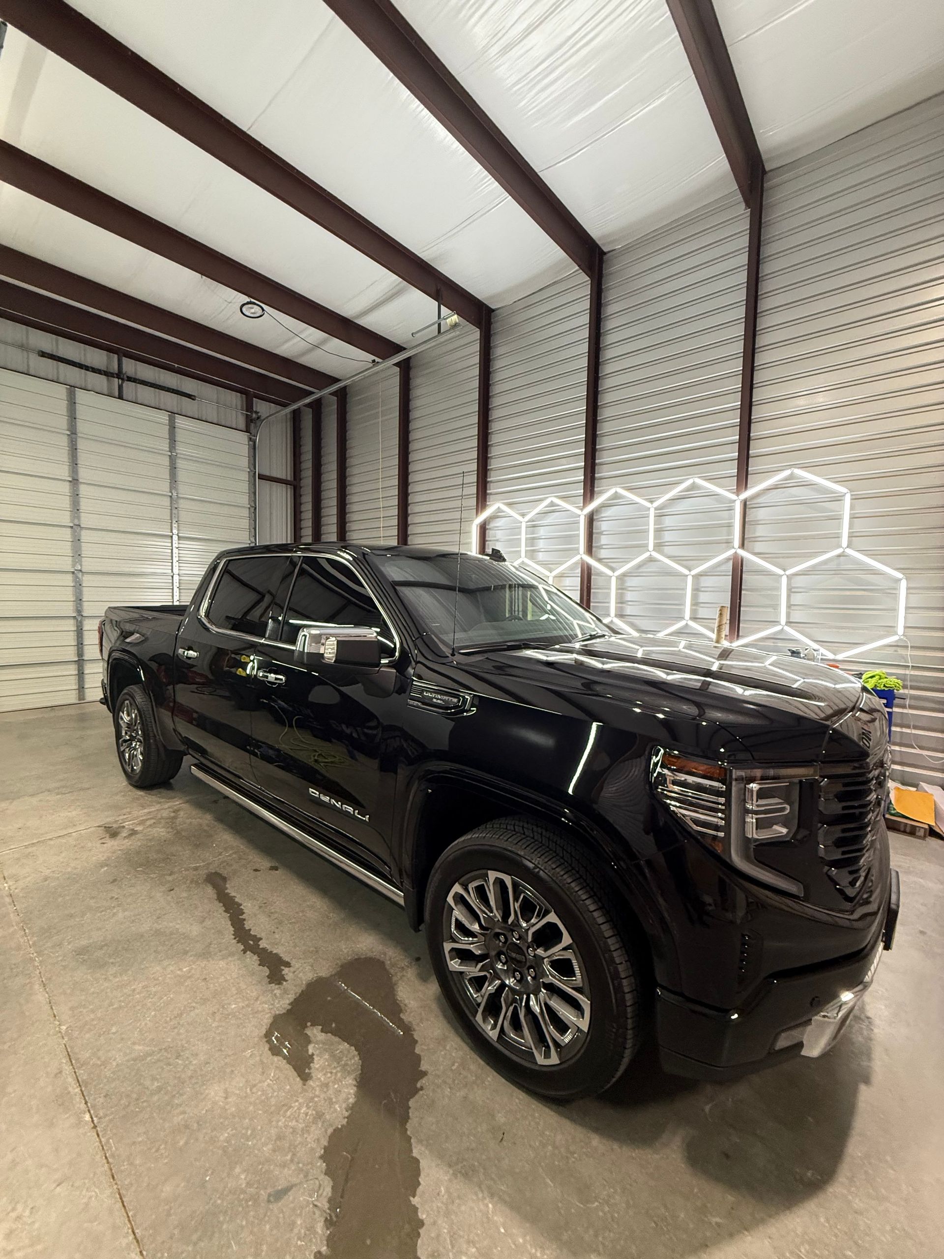 Black GMC Sierra truck inside a garage with white walls and hexagonal lighting.