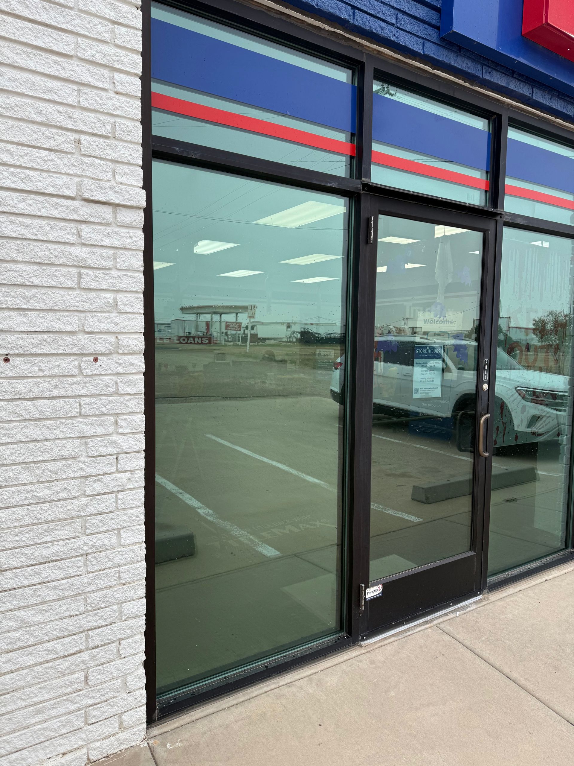 Exterior of a building with glass doors and windows, reflecting a parking lot and gas station.