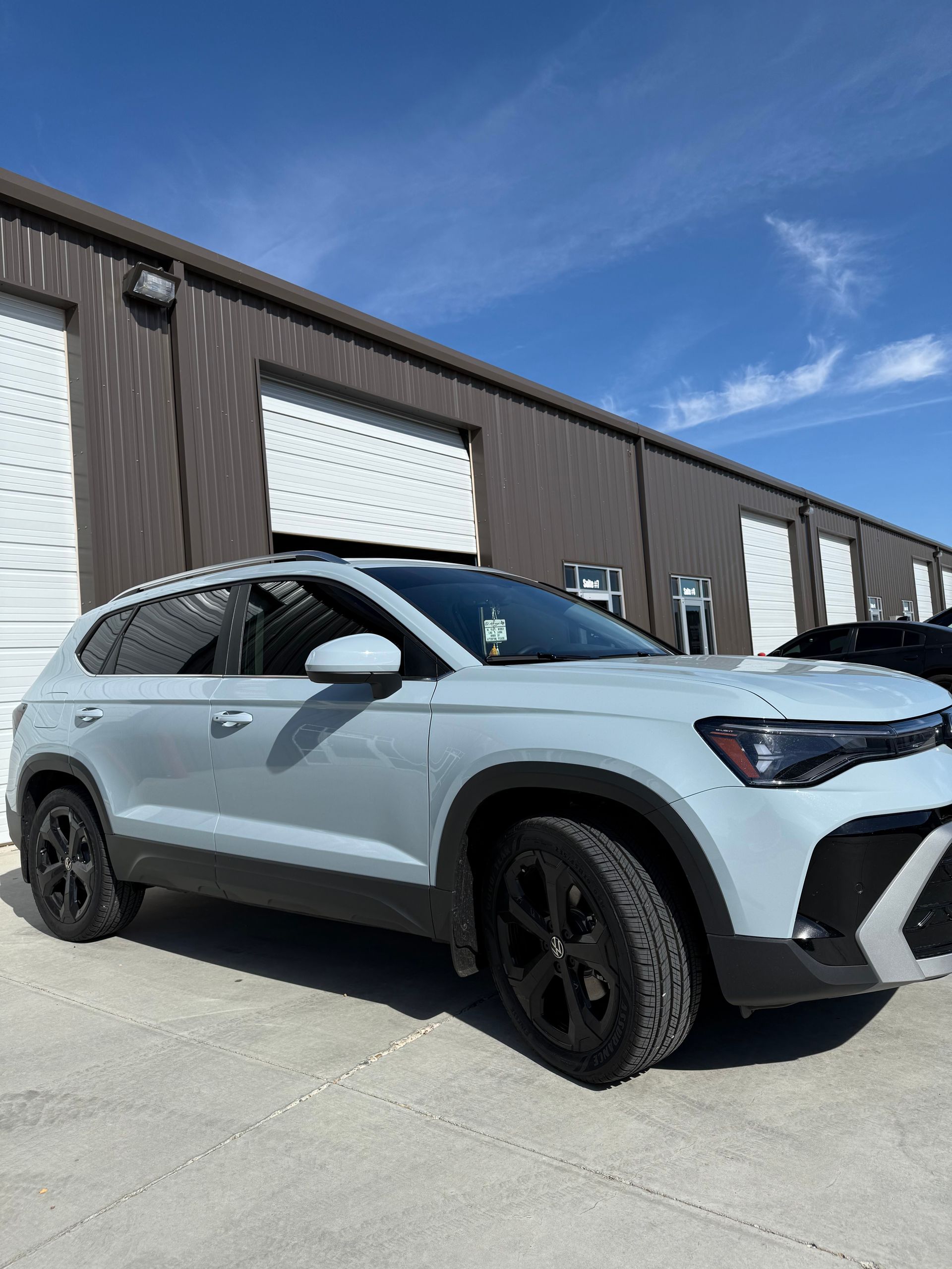 Light gray SUV parked in front of a brown building with a blue sky background. Black wheels and trim.