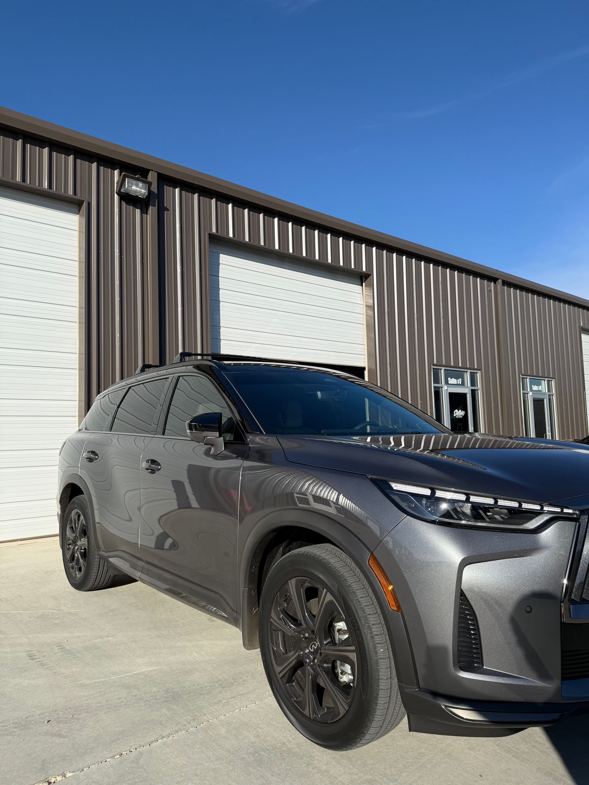 Gray SUV parked in front of a metal building with white garage doors under a blue sky.