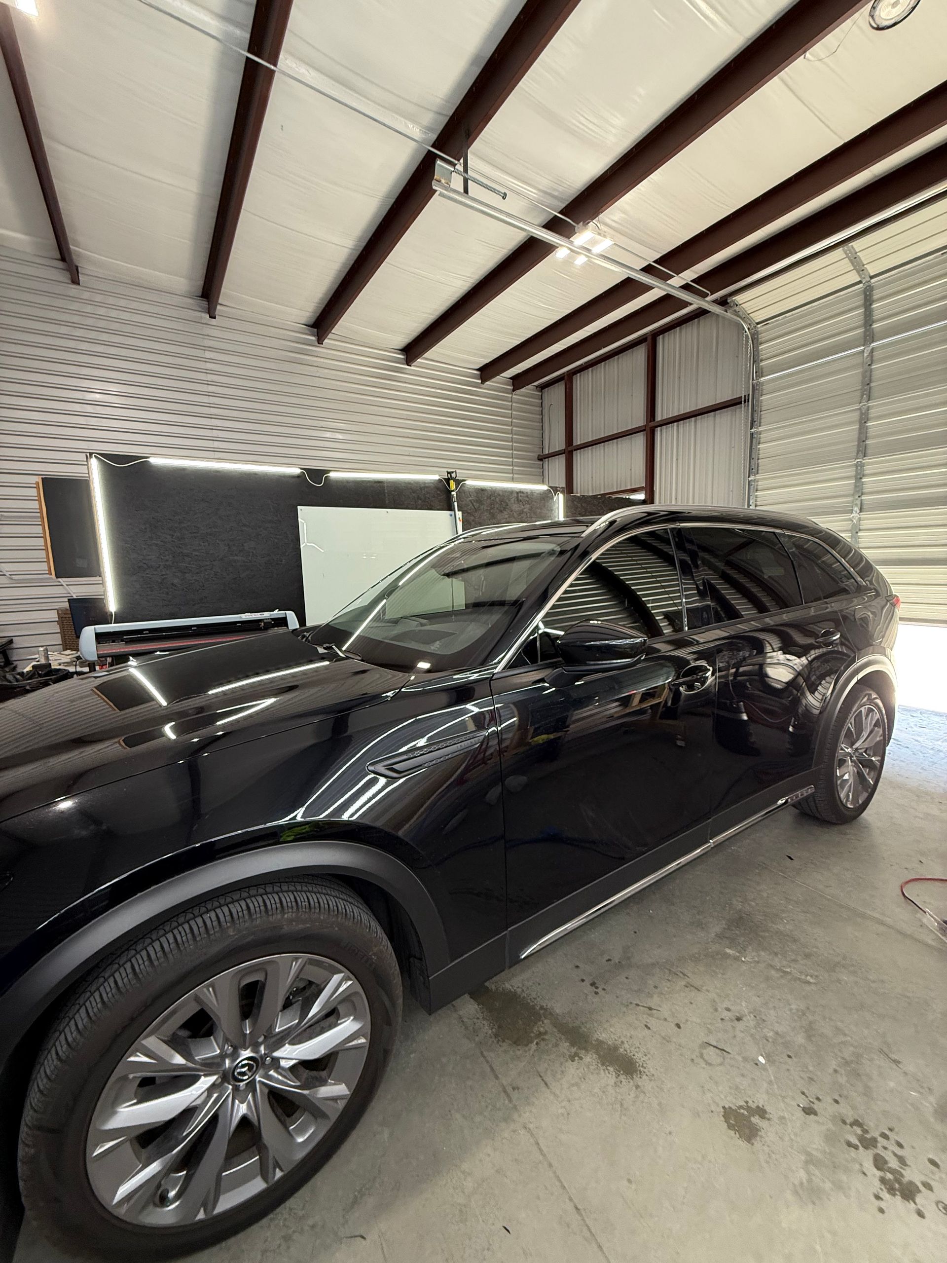 Black SUV parked inside a garage. Metal roof and door visible, car wheels and body in focus.