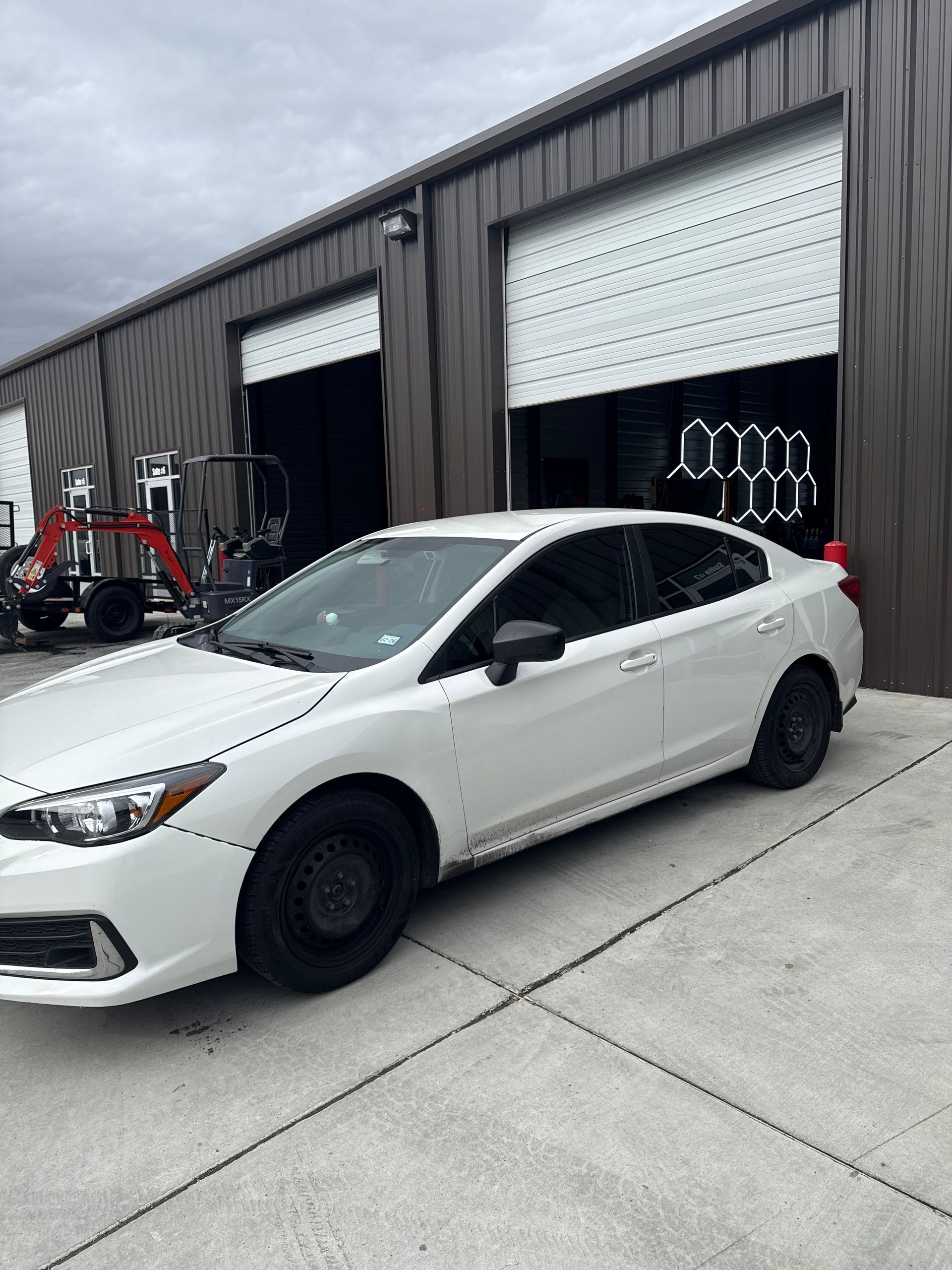 White Subaru sedan parked in front of a building with open garage doors.