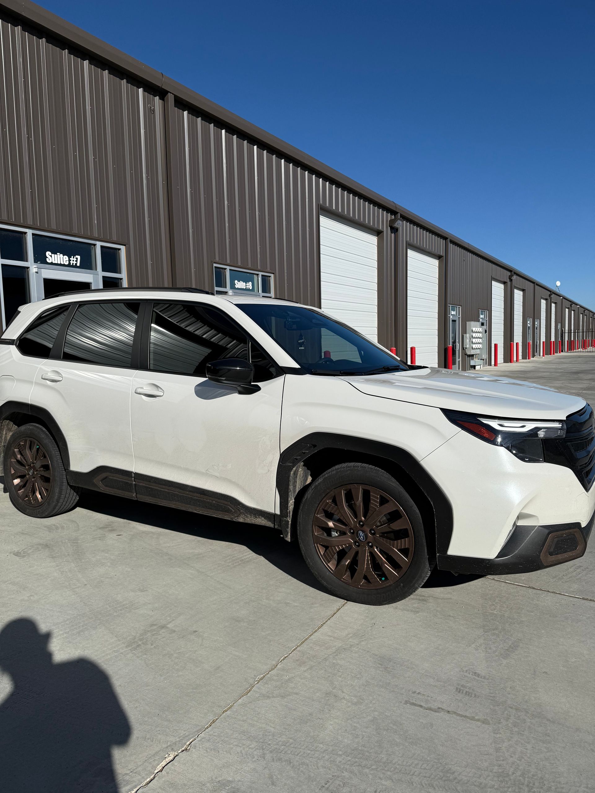 White SUV with brown wheels parked in front of a metal building on a sunny day.