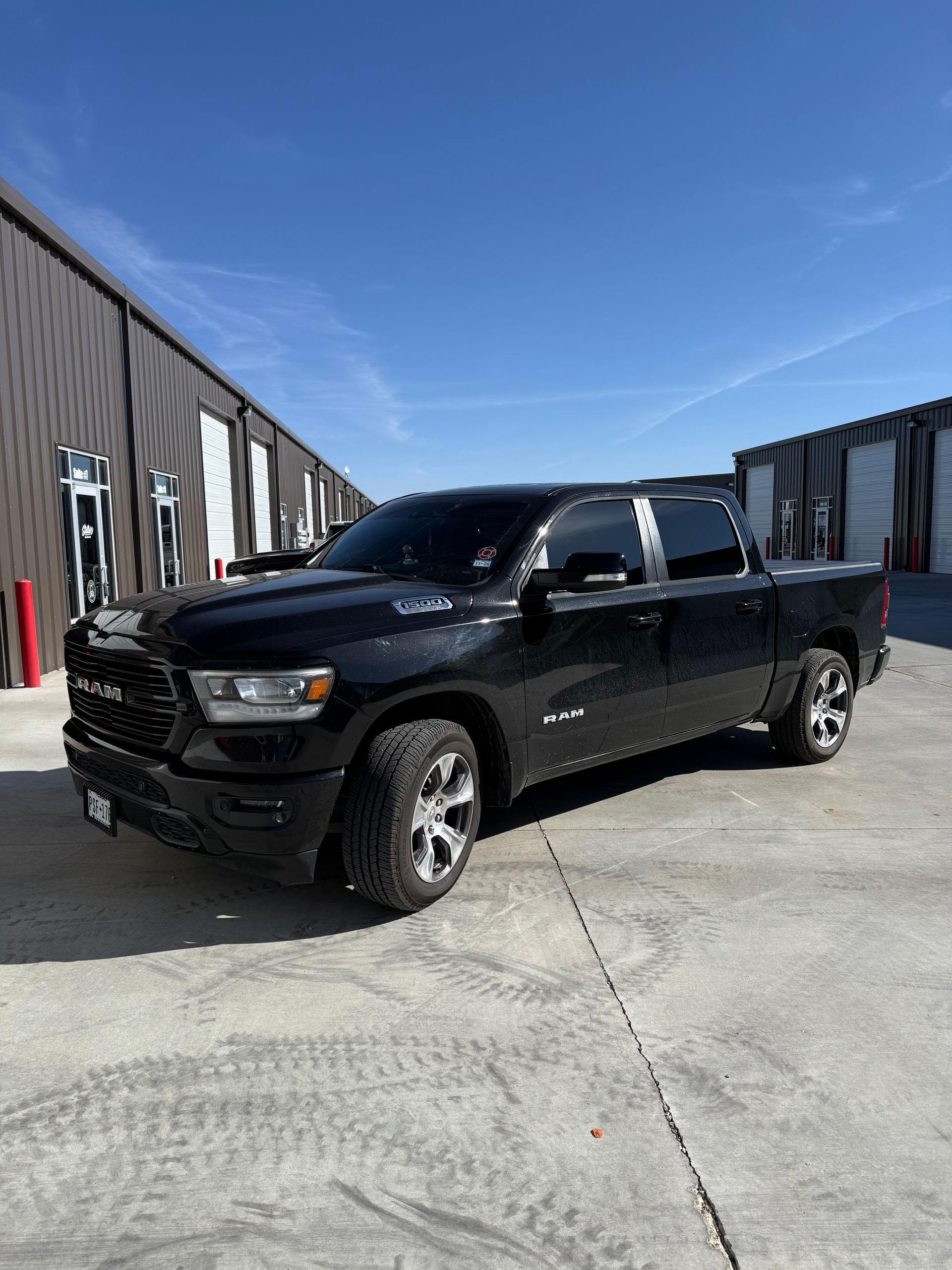 Black Dodge Ram pickup truck parked in front of storage units under a clear blue sky.