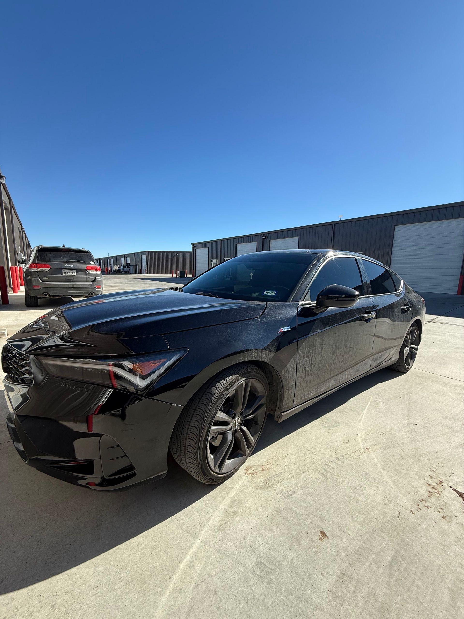 Black Acura Integra parked on concrete, with damage to the front. Clear, sunny sky in the background.