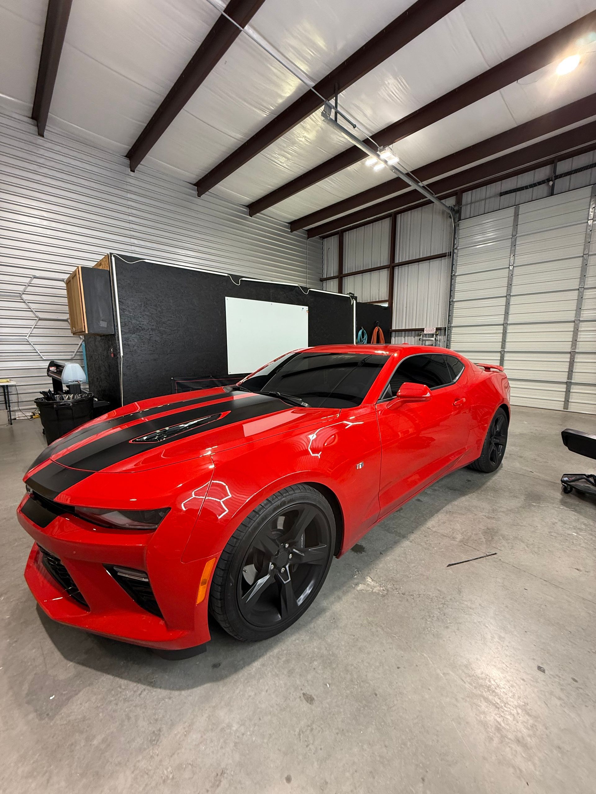 Red Chevrolet Camaro with black racing stripes in a garage.