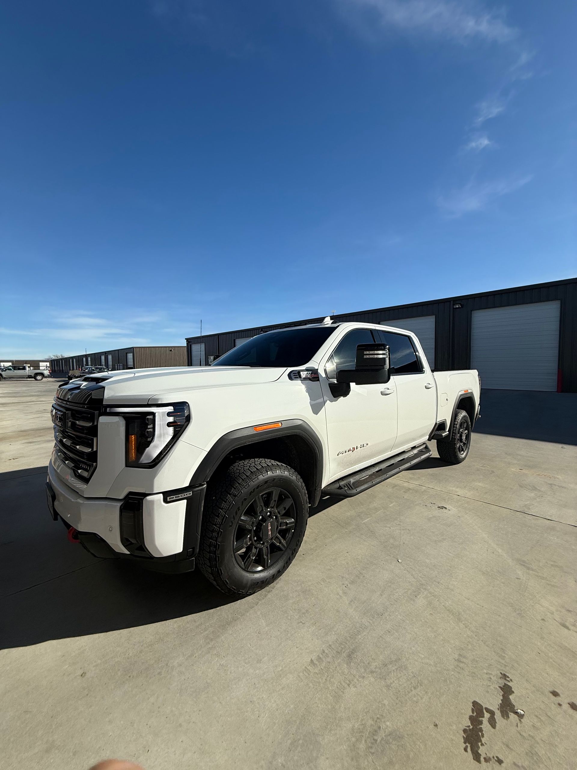 White GMC Sierra truck with black wheels parked outside on a sunny day.