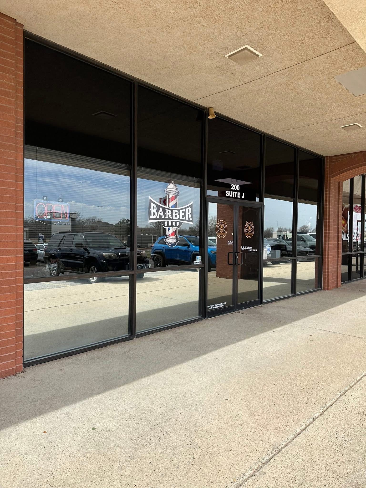 Barbershop storefront with large windows reflecting cars and the sky. The shop has a sign with 